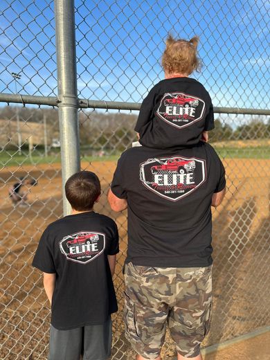 A man carrying a child on his shoulders wearing a shirt that says elite