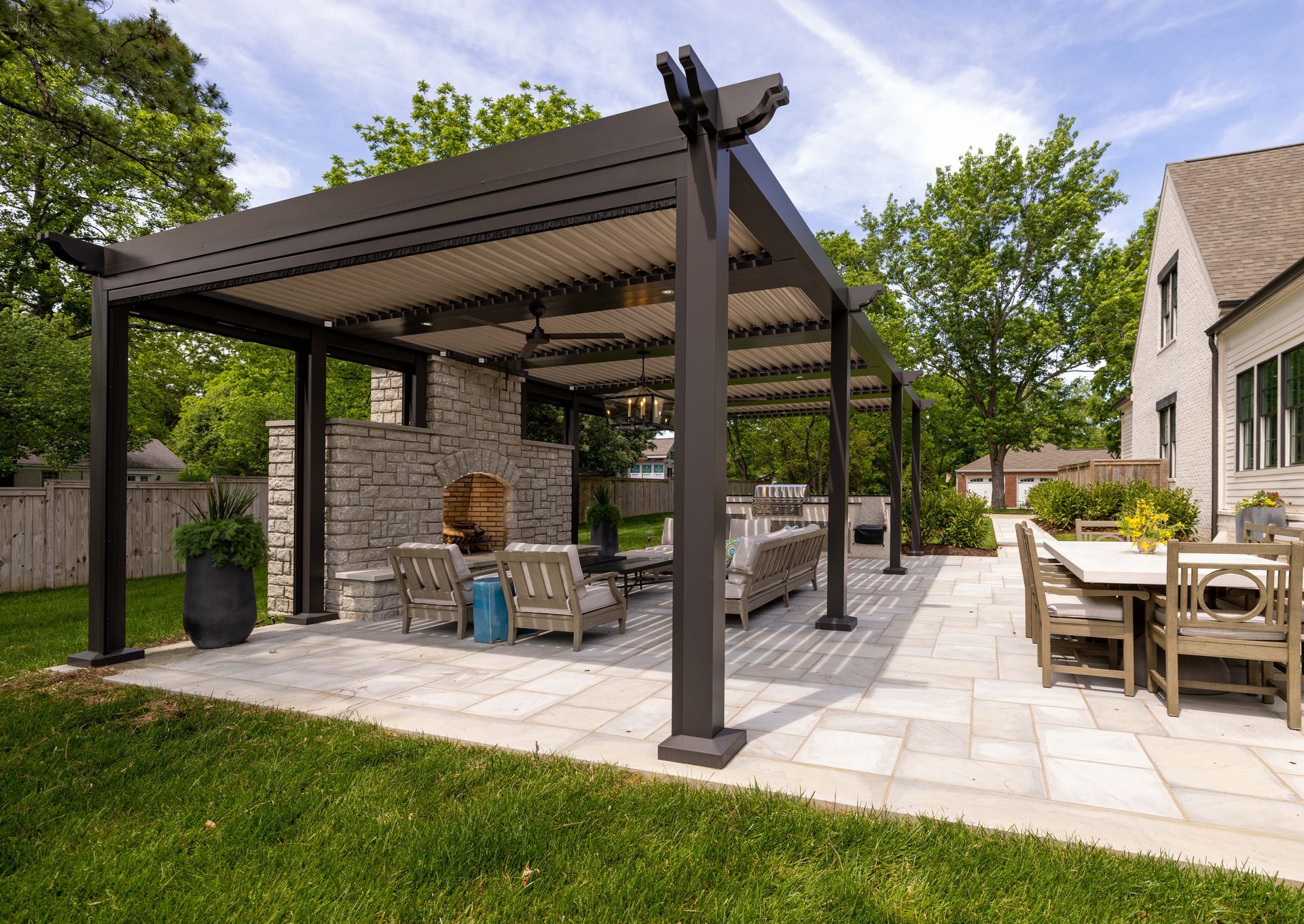Outdoor patio with pergola, fireplace, and dining table on a sunny day.