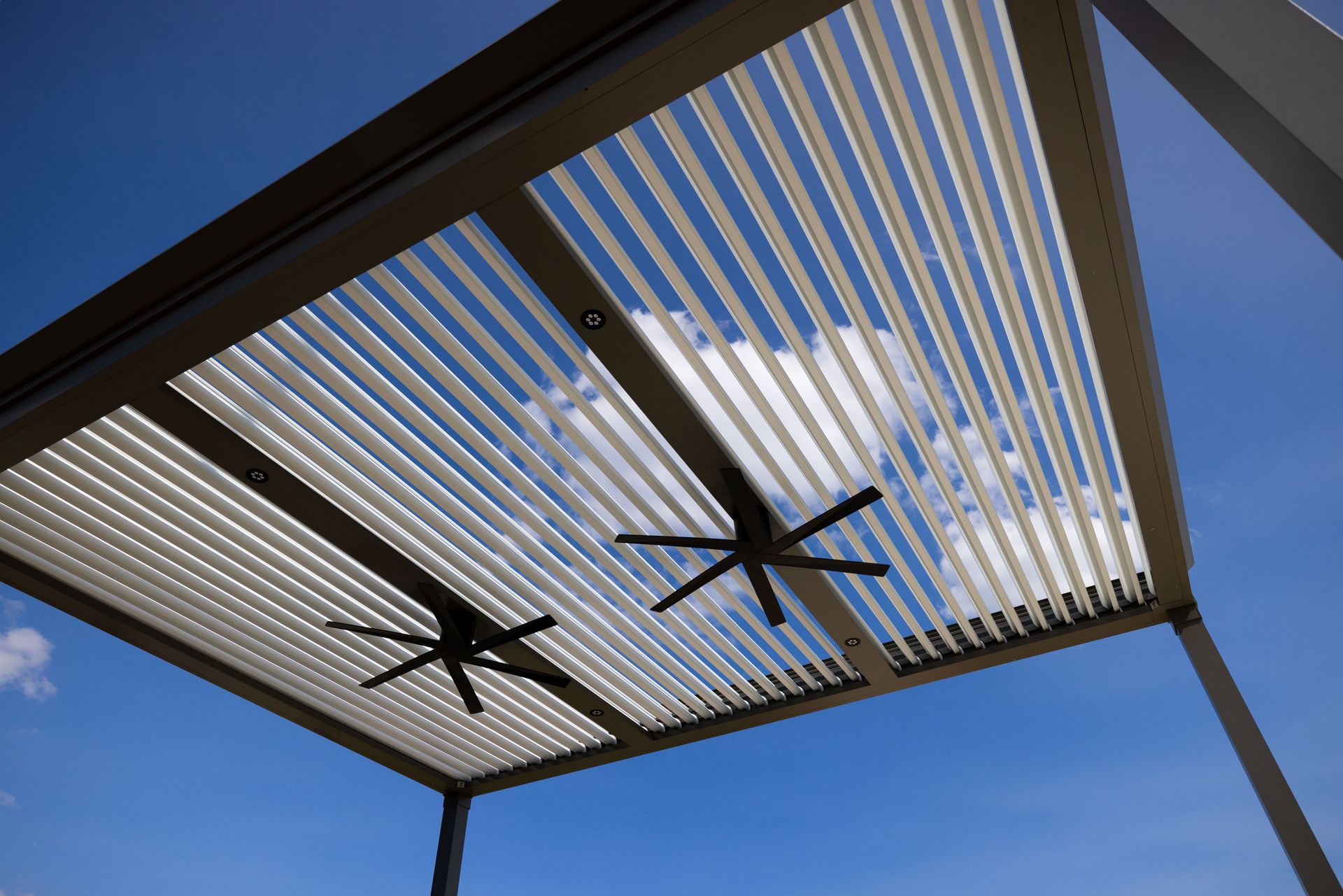 Pergola with slatted roof, two ceiling fans, against a blue sky.