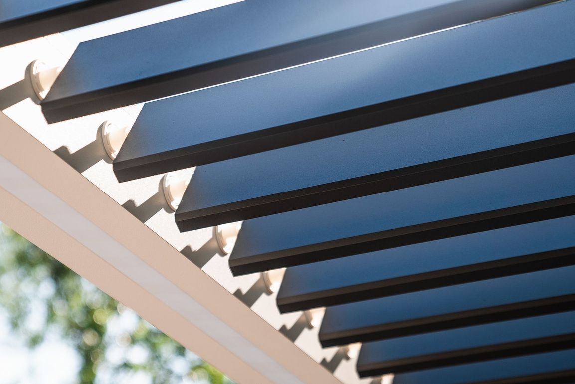 Black, horizontal slats of a pergola cast shadows onto a cream-colored frame.