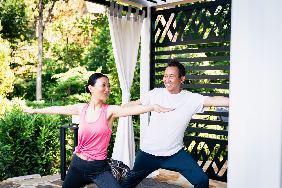 Two people doing yoga outside. One in pink, one in white, arms outstretched, smiling.