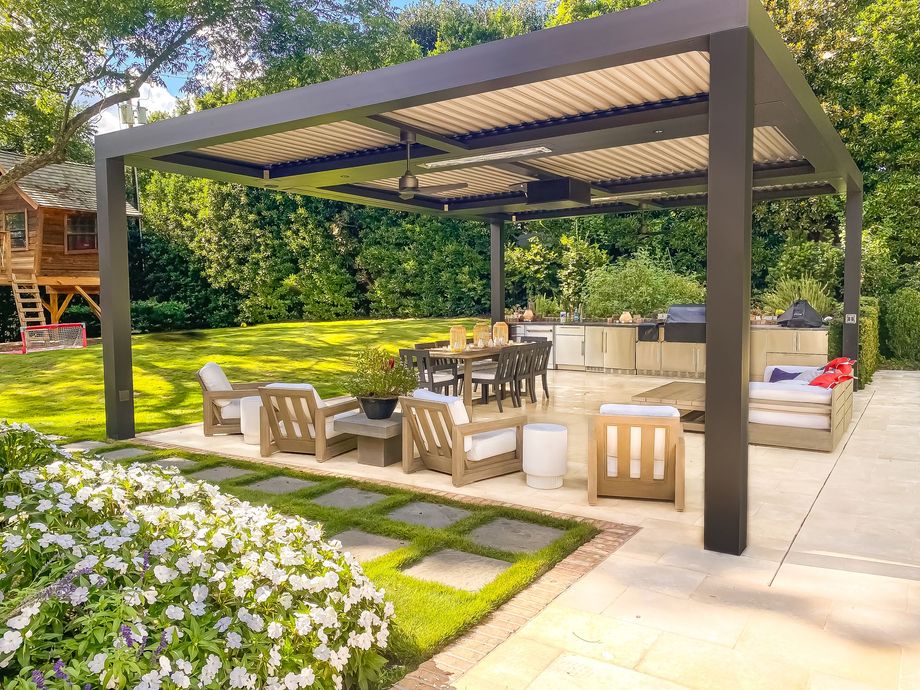 Outdoor patio with pergola, seating area, dining table, and built-in grill, surrounded by greenery.