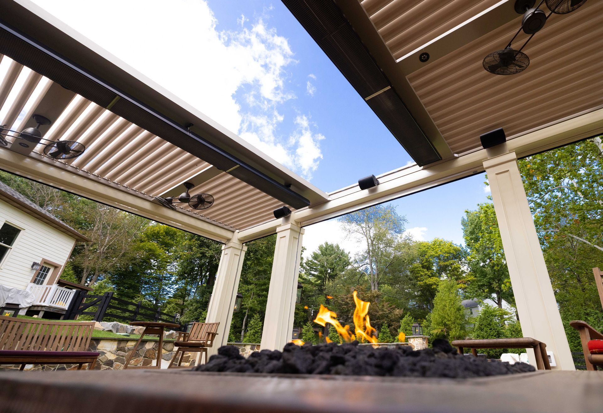 Outdoor patio with fire pit, slatted roof, white pillars, and blue sky.