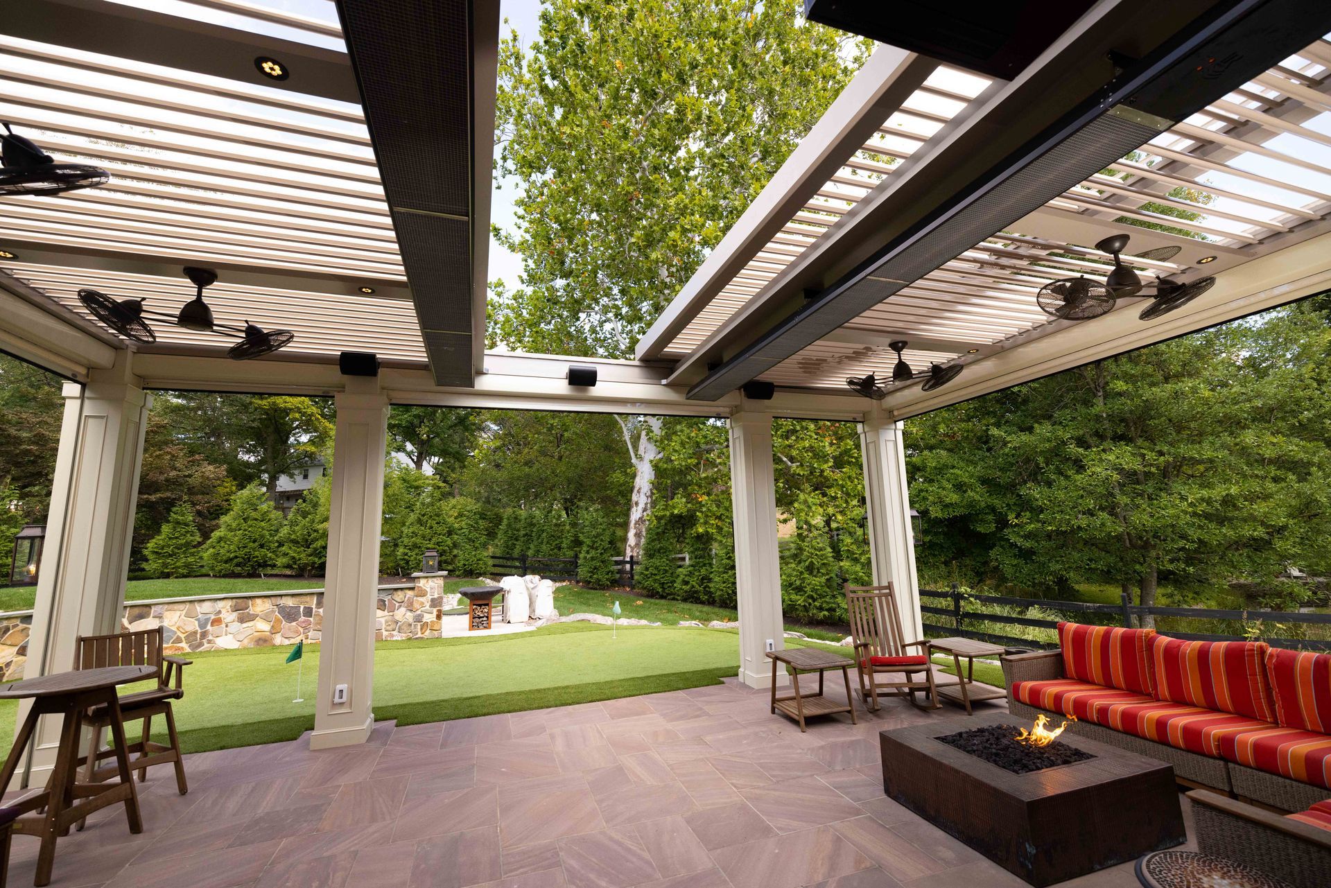 Patio with a stone floor, outdoor fireplace, seating area, and overhead pergola with fans.