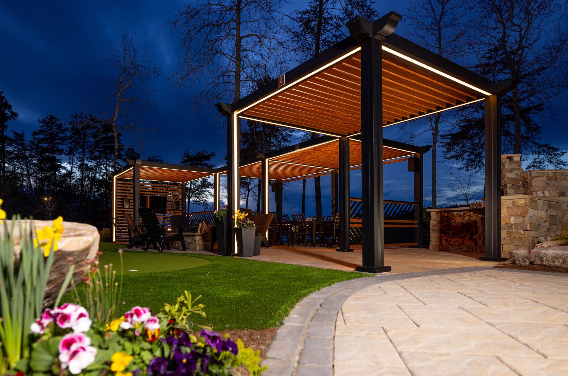 Outdoor dining area with illuminated pergolas at dusk, with flowers in foreground.