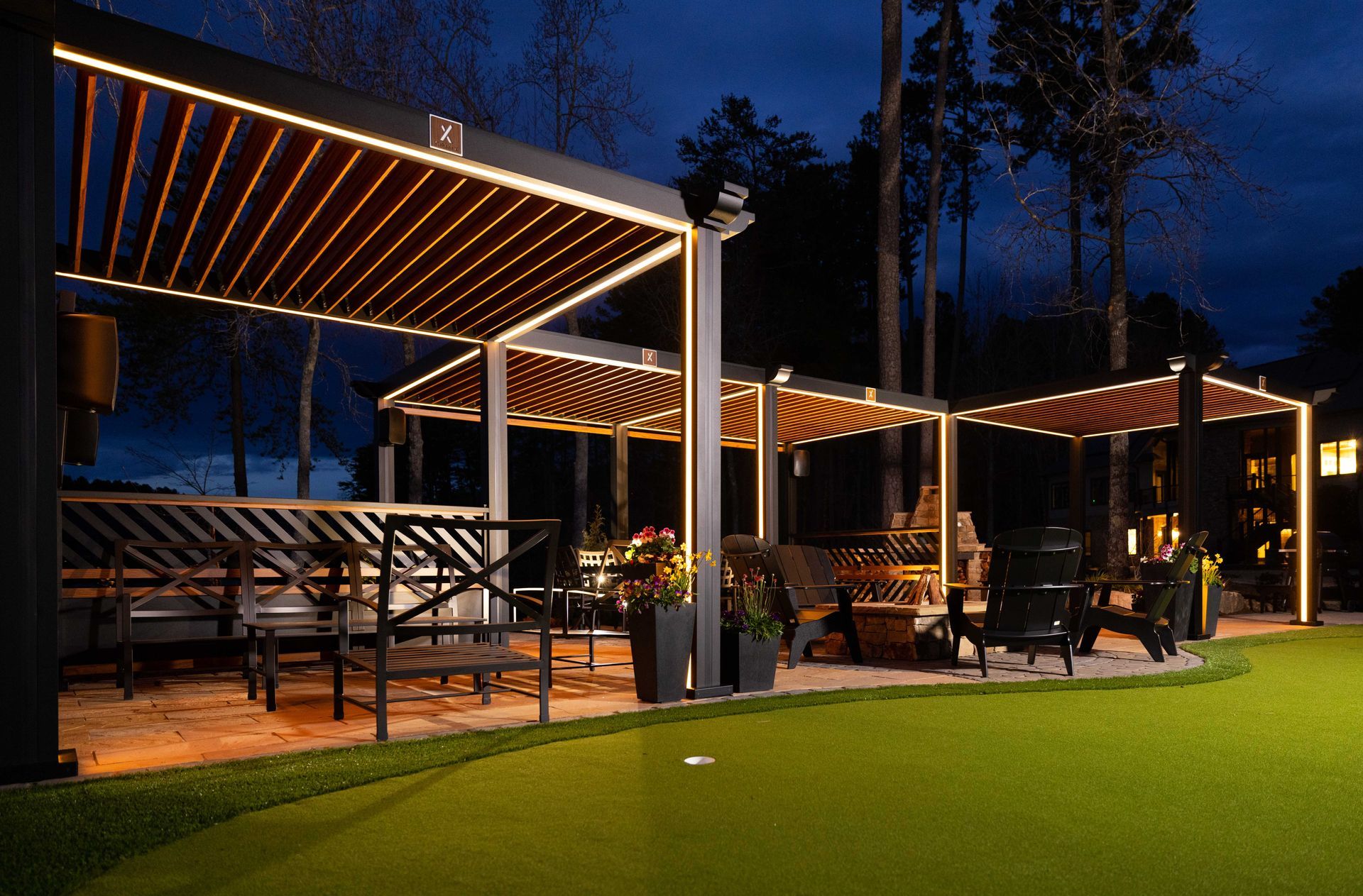 Outdoor patio with lit pergola structures at night, over a putting green.