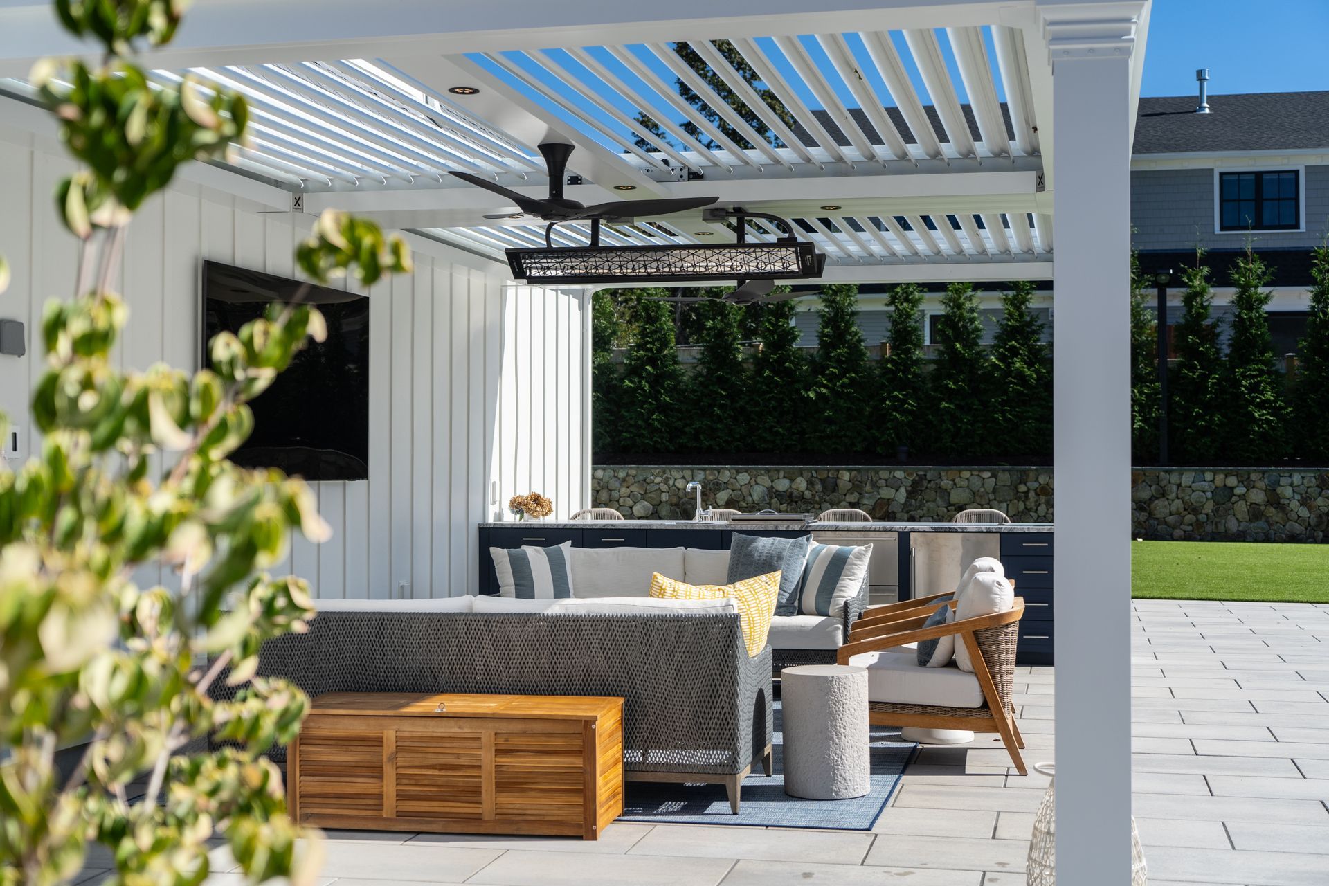 Outdoor patio with seating, kitchen, and TV under a white pergola.