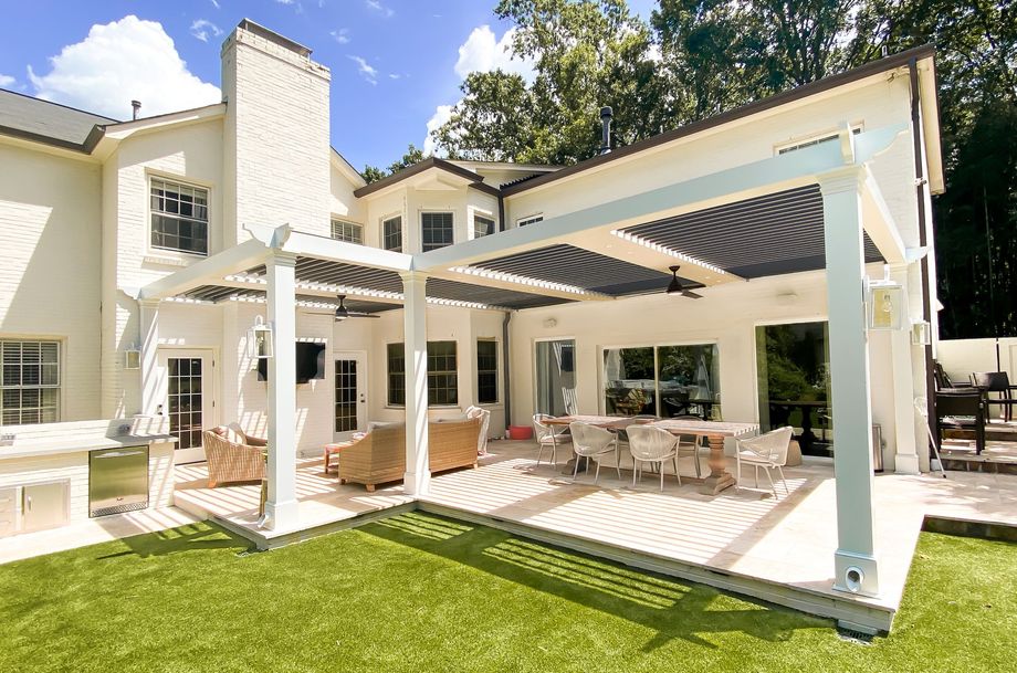 Backyard patio with white pergola, outdoor seating, and green grass.