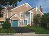 Two-story beige brick house with teal garage door and front door, black asphalt driveway, and green grass.