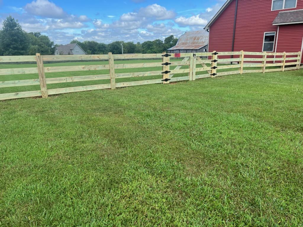 A wooden fence surrounds a lush green field in front of a red house. Clarksville, TN