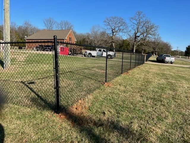 A chain link fence is surrounding a grassy field with a house in the background. Clarksville, TN