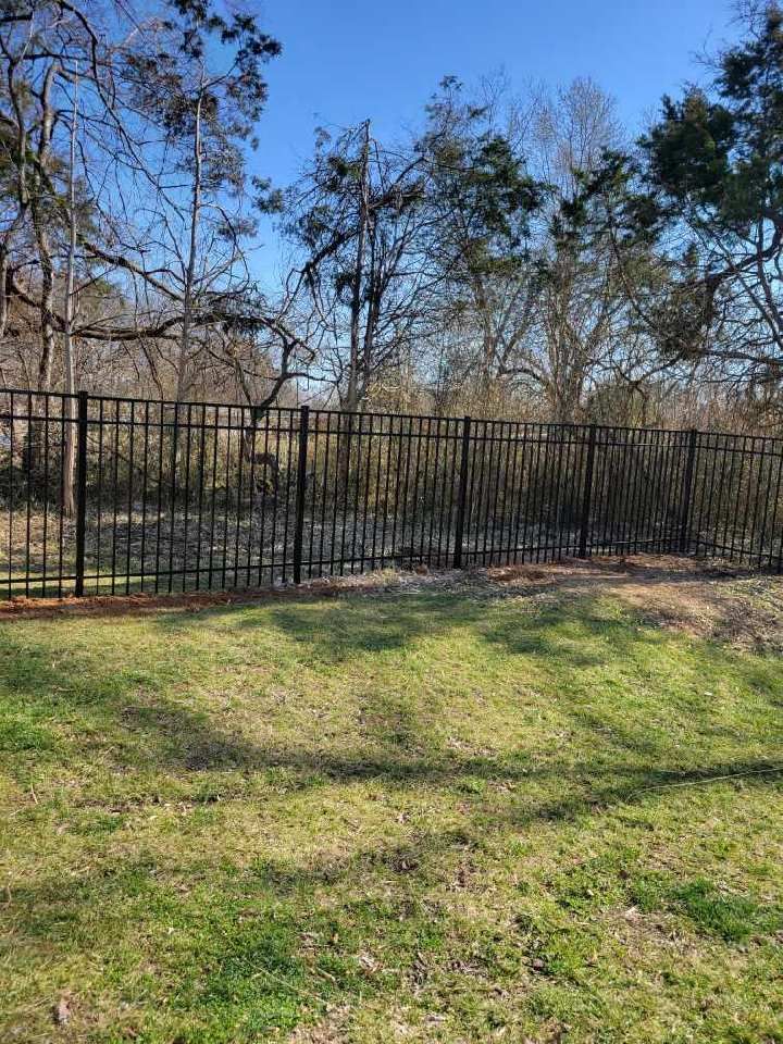A black fence surrounds a lush green field with trees in the background. Middle, TN