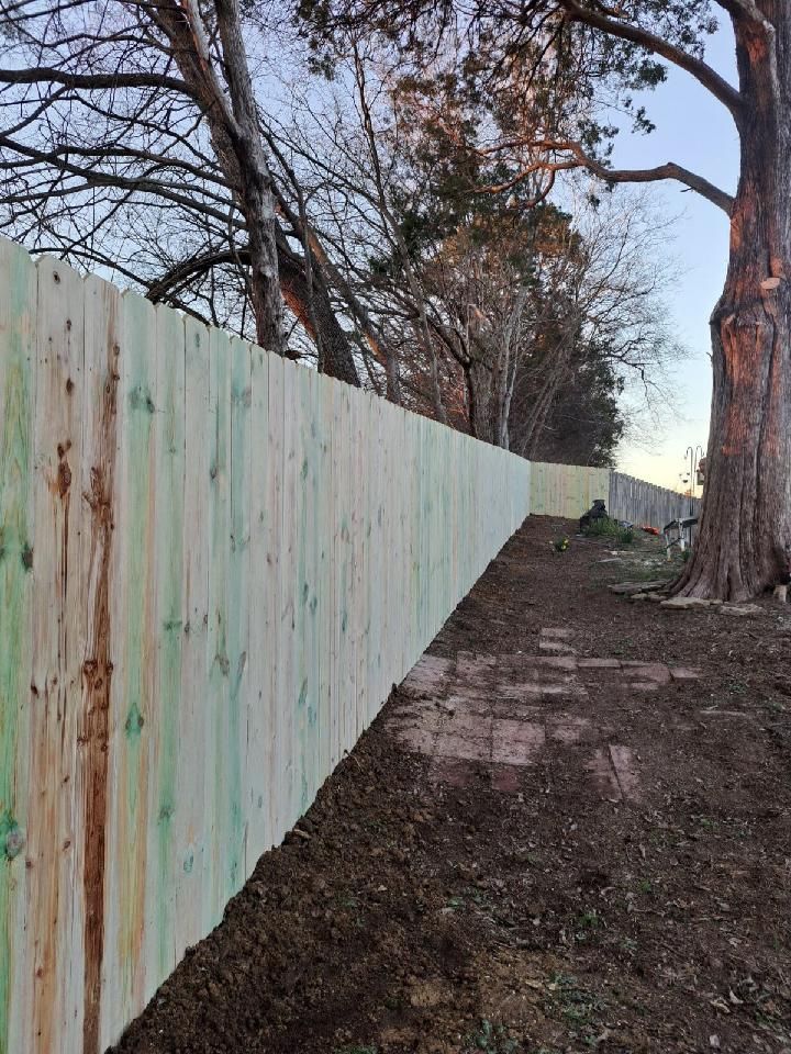 A wooden fence is surrounded by trees and dirt in a yard. Middle, TN