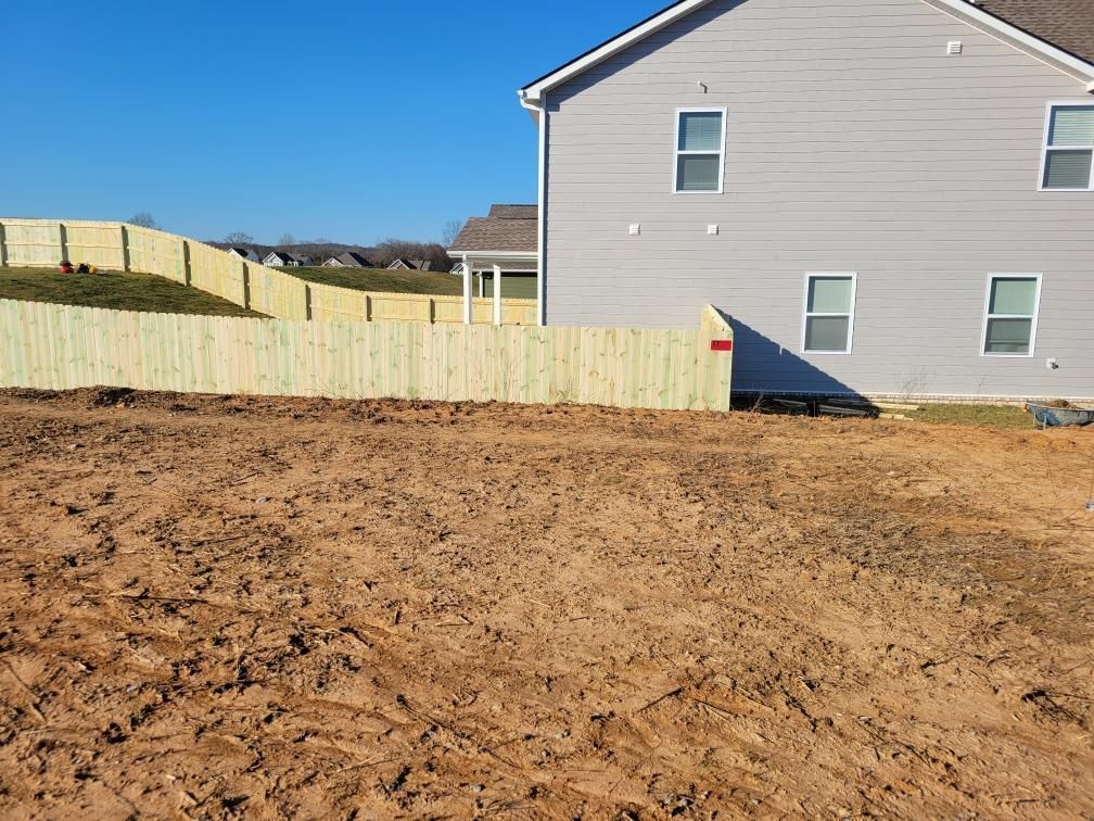 A house with a wooden fence in front of it and a dirt field in front of it. Middle, TN