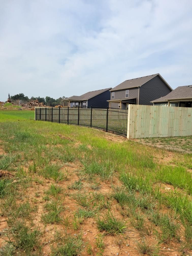 A wooden fence surrounds a grassy field with houses in the background. Middle, TN