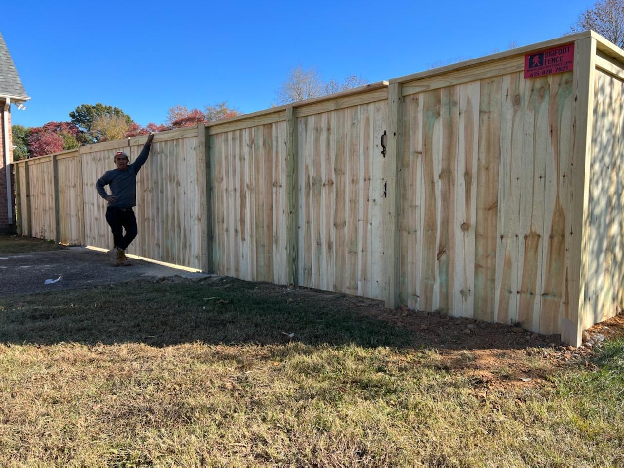 A man is standing next to a wooden fence in a yard. Middle, TN