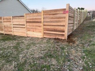 A wooden fence is sitting on top of a grassy hill next to a house. Clarksville, TN