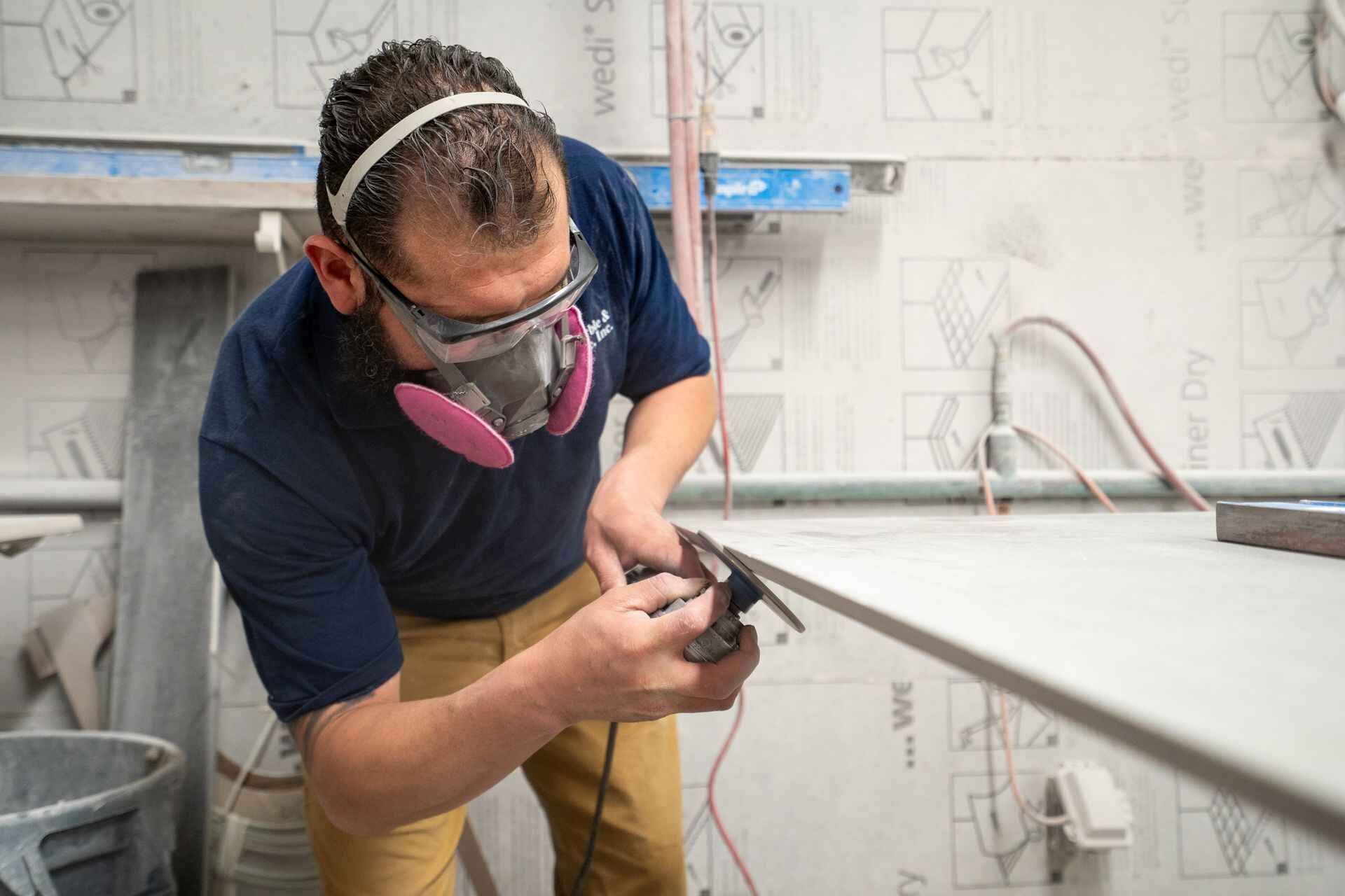A man wearing a mask and goggles is sanding a piece of wood.