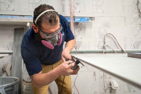 A man wearing a mask and goggles is sanding a piece of wood.