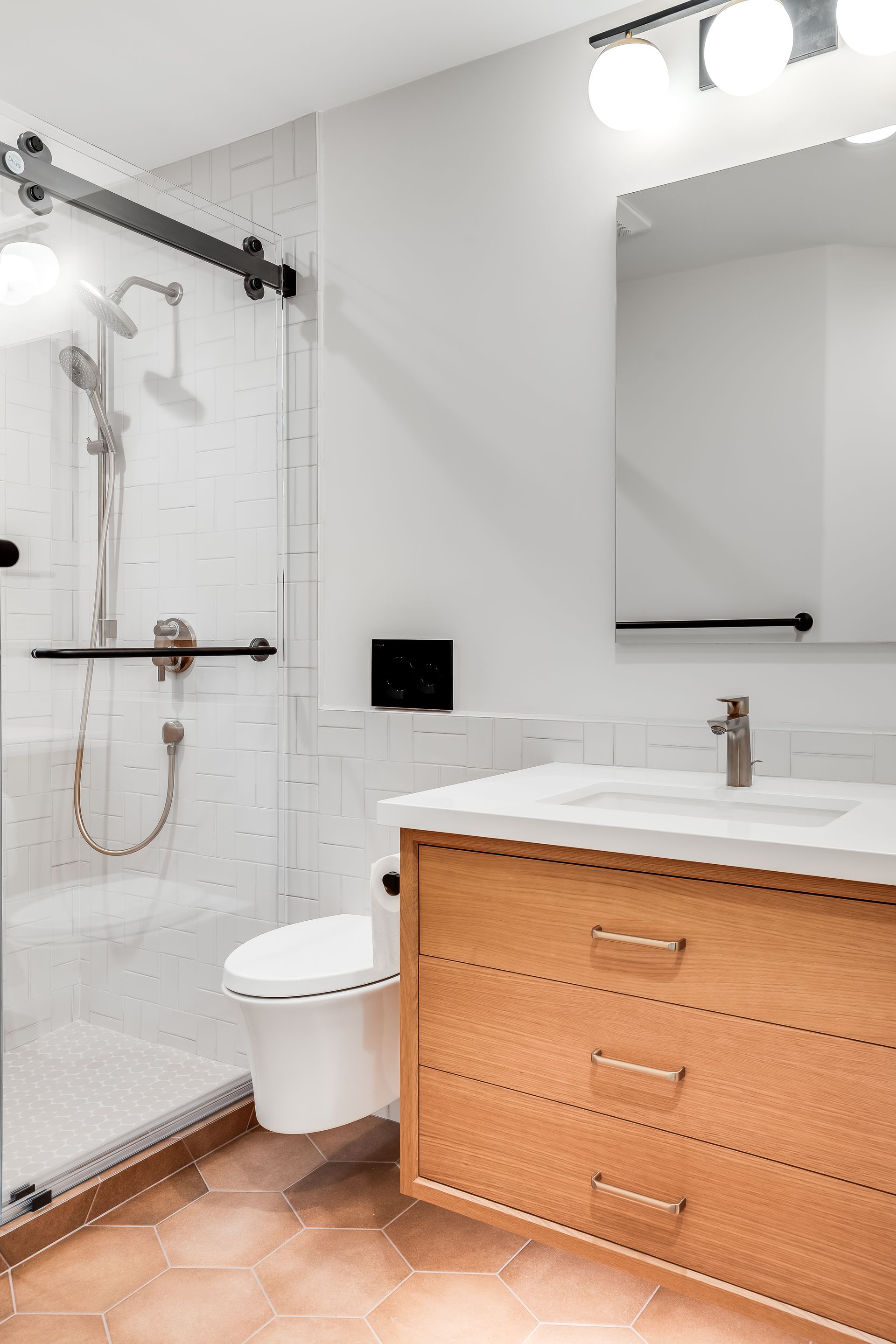 Modern bathroom with a light wood vanity, white walls, and a glass shower.