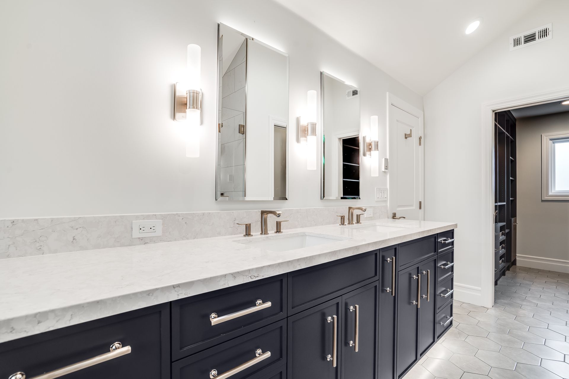 Modern bathroom with navy cabinets, white countertop, and three mirrors with sconces.