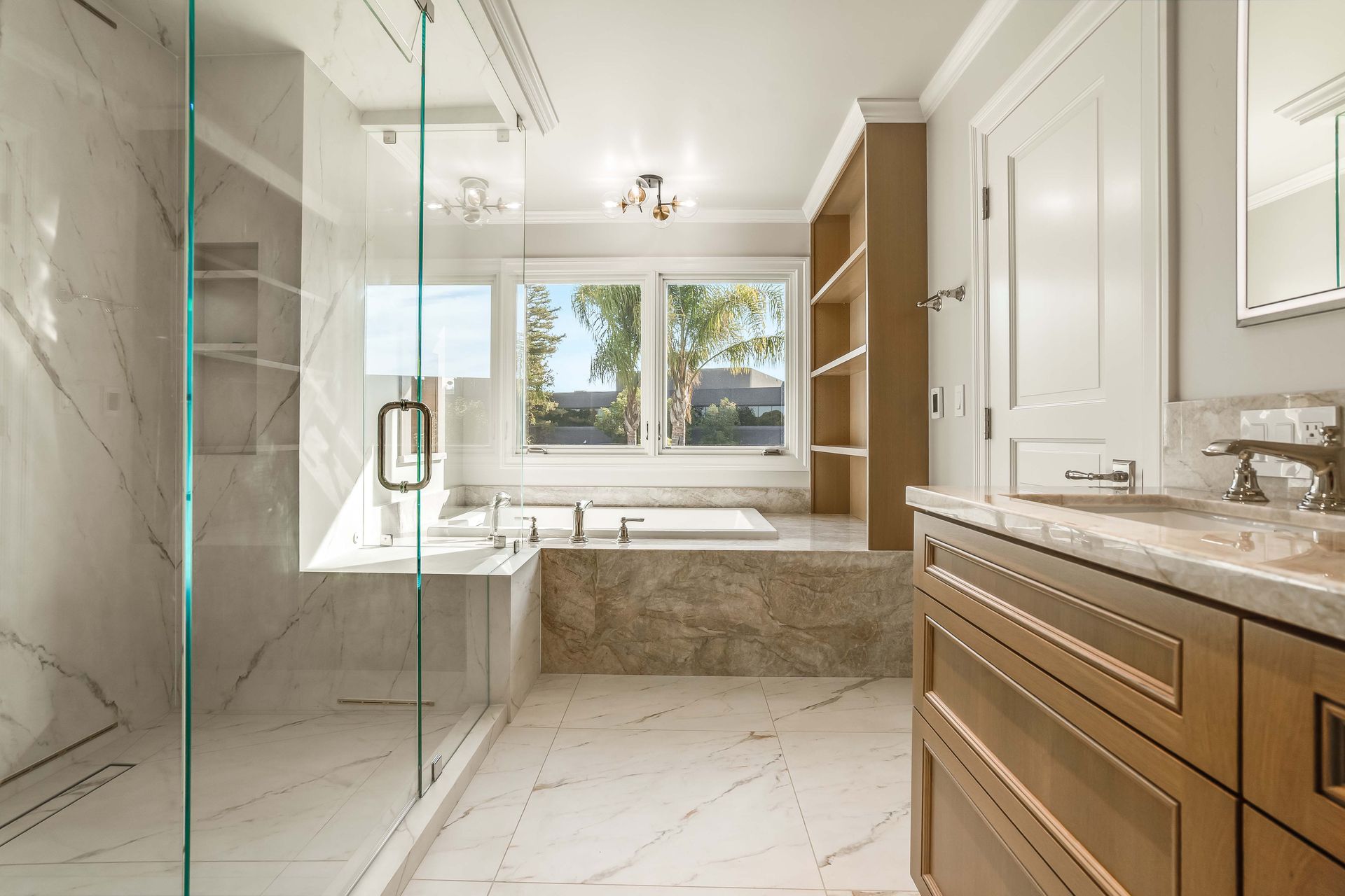 Luxurious bathroom with marble tile, glass shower, built-in tub, and wooden vanity.