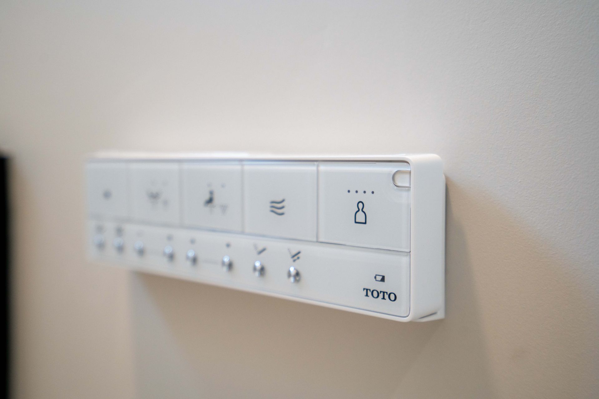 White control panel on a wall with multiple buttons and symbols for a toilet, likely a bidet control.