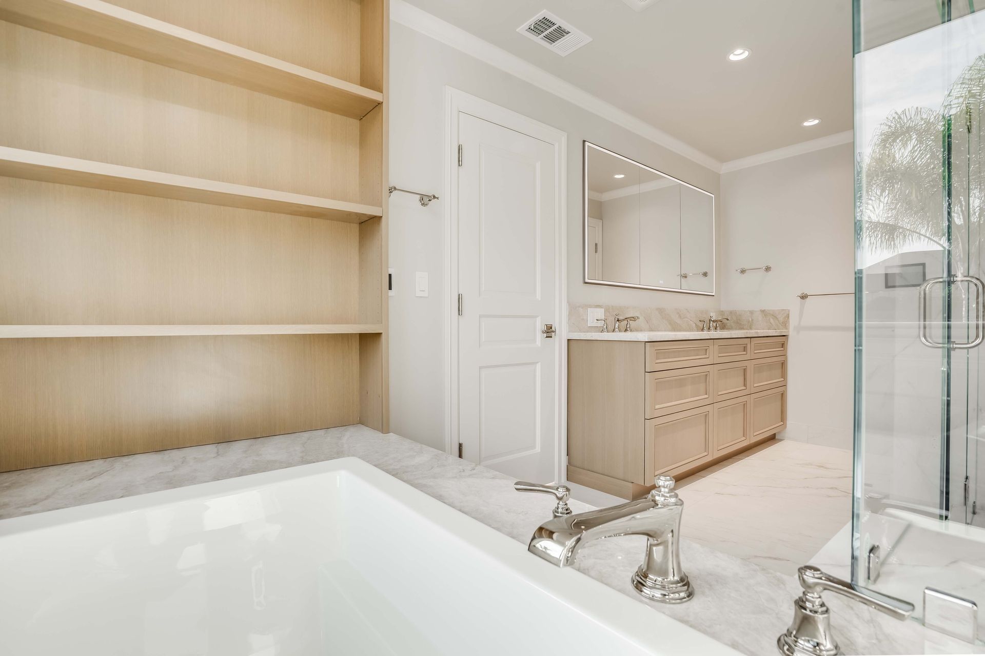 Bathroom with built-in shelves, bathtub, vanity, and a glass-enclosed shower. Neutral tones and marble floors.