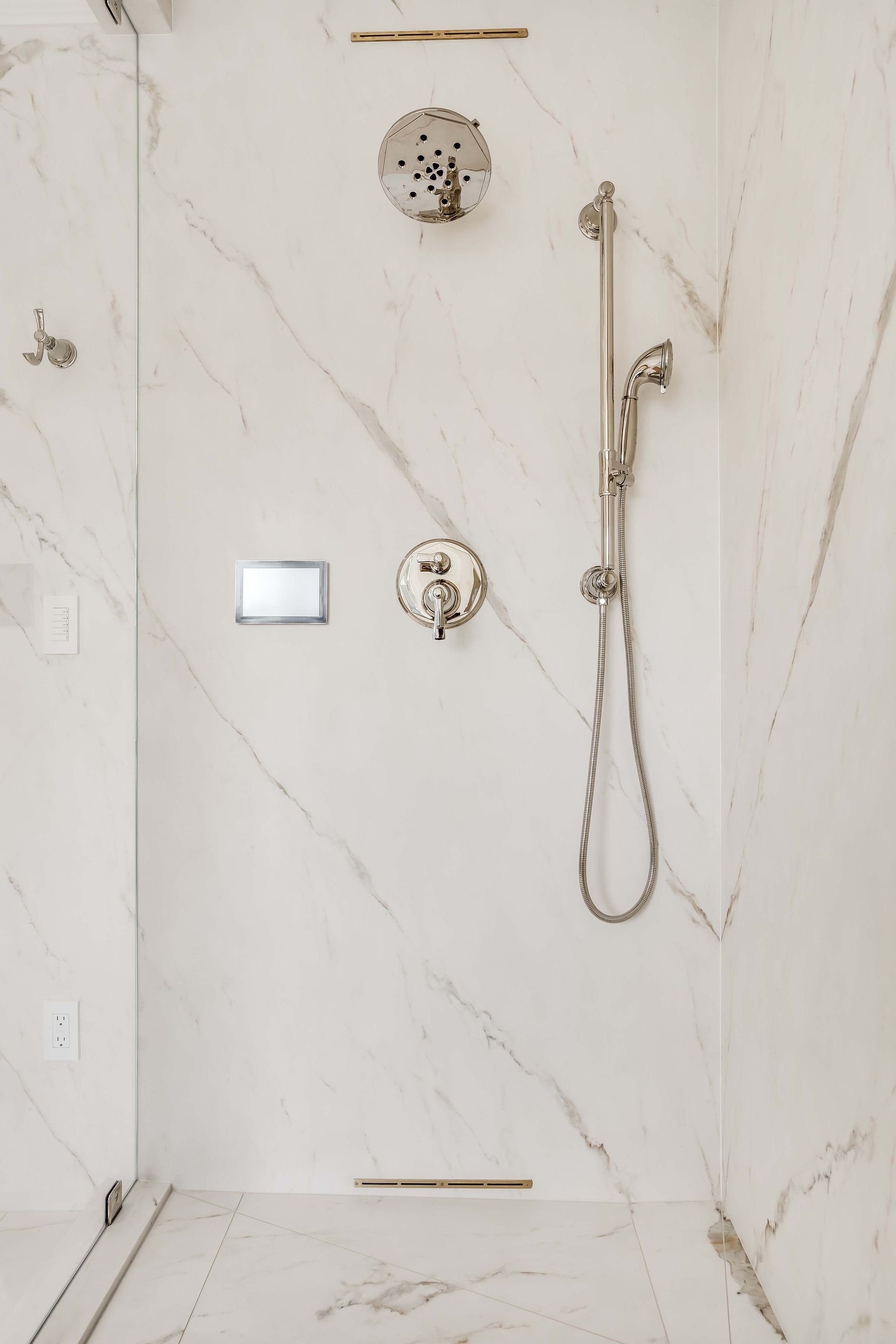 Shower with white marble walls and silver fixtures.