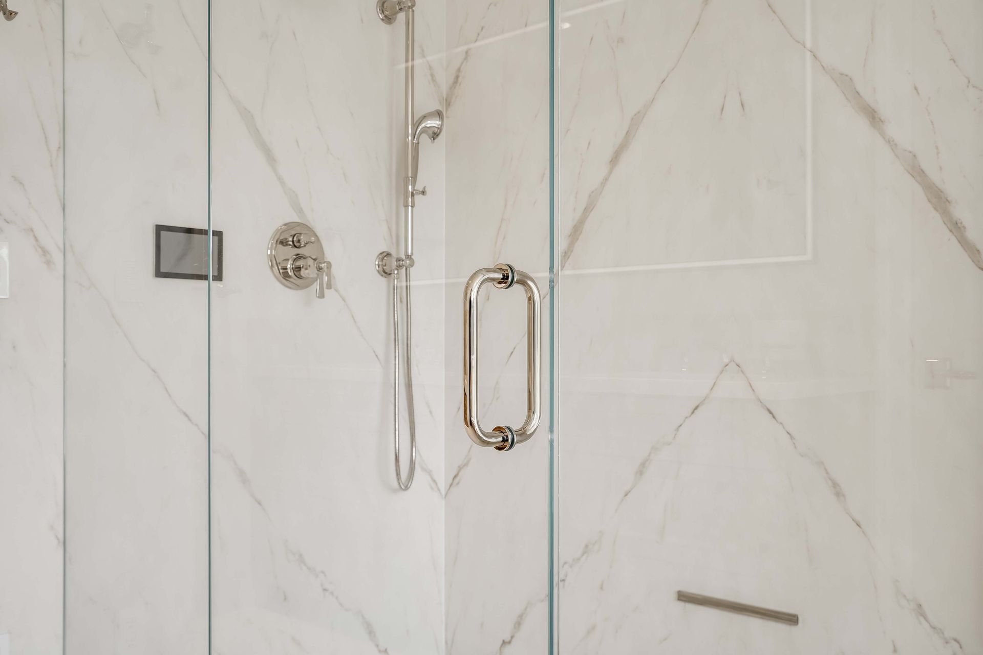 Glass shower enclosure with white marble-look tile and silver fixtures.