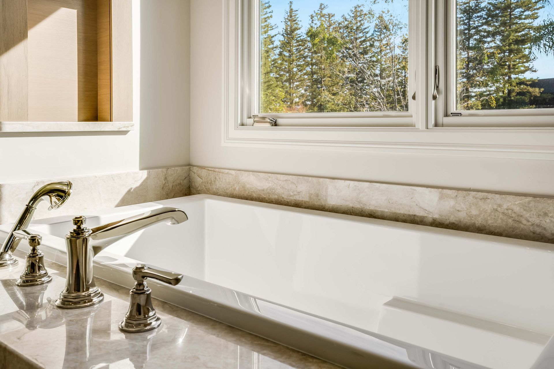 White bathtub with chrome fixtures near a window overlooking trees.