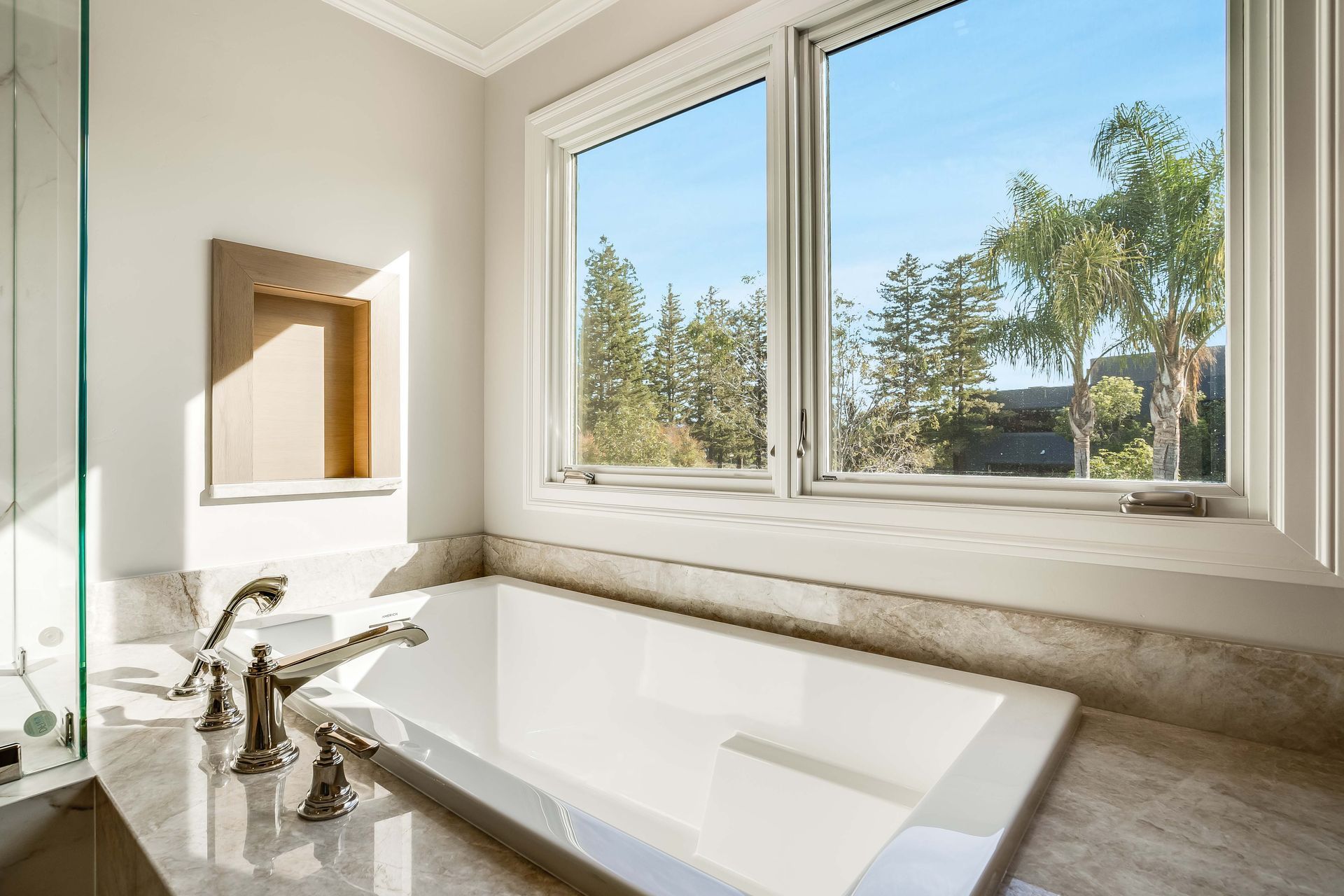 Bathroom with rectangular tub, window overlooking trees, and marble surfaces.