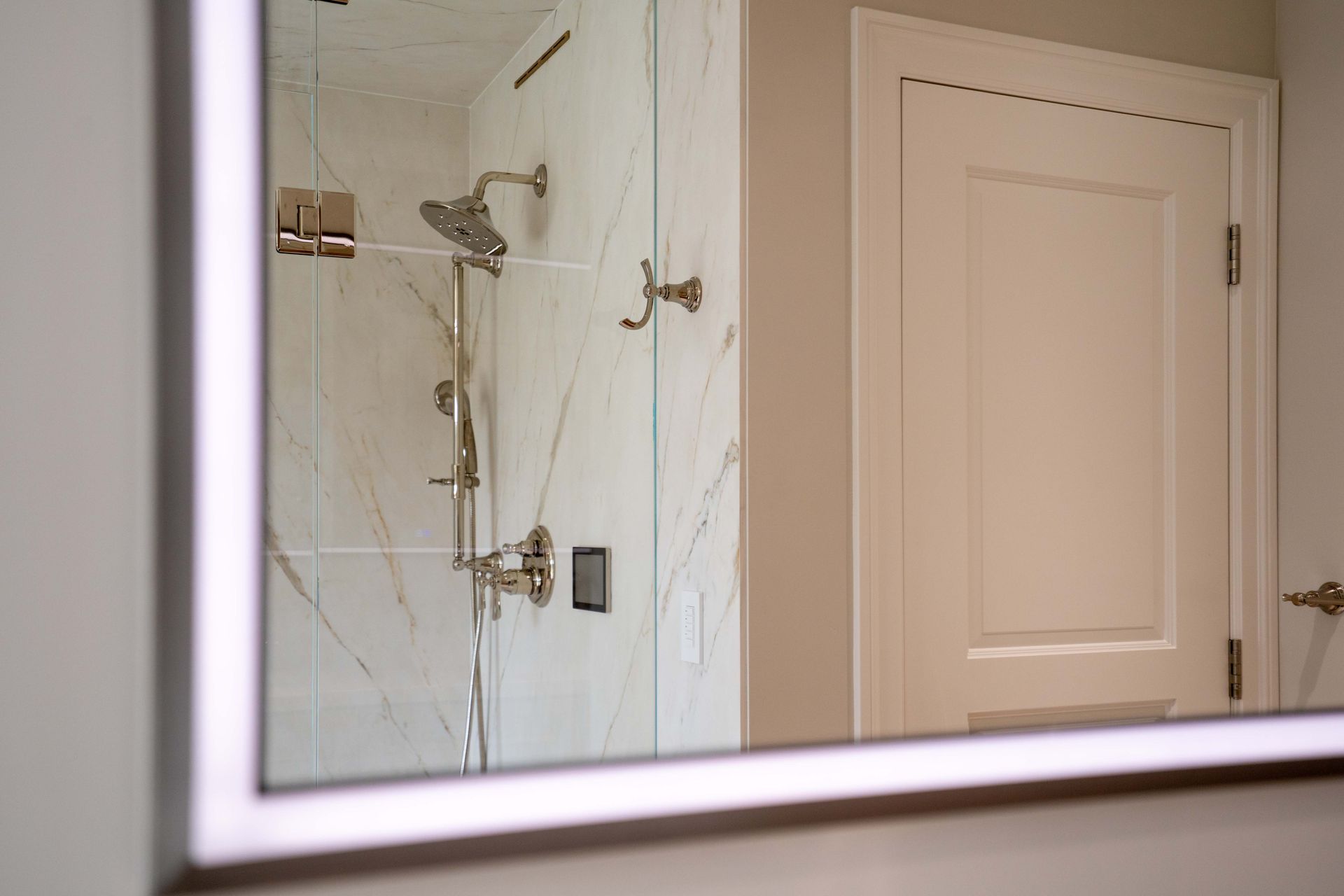 Mirror reflecting a marble shower and a white door in a modern bathroom.