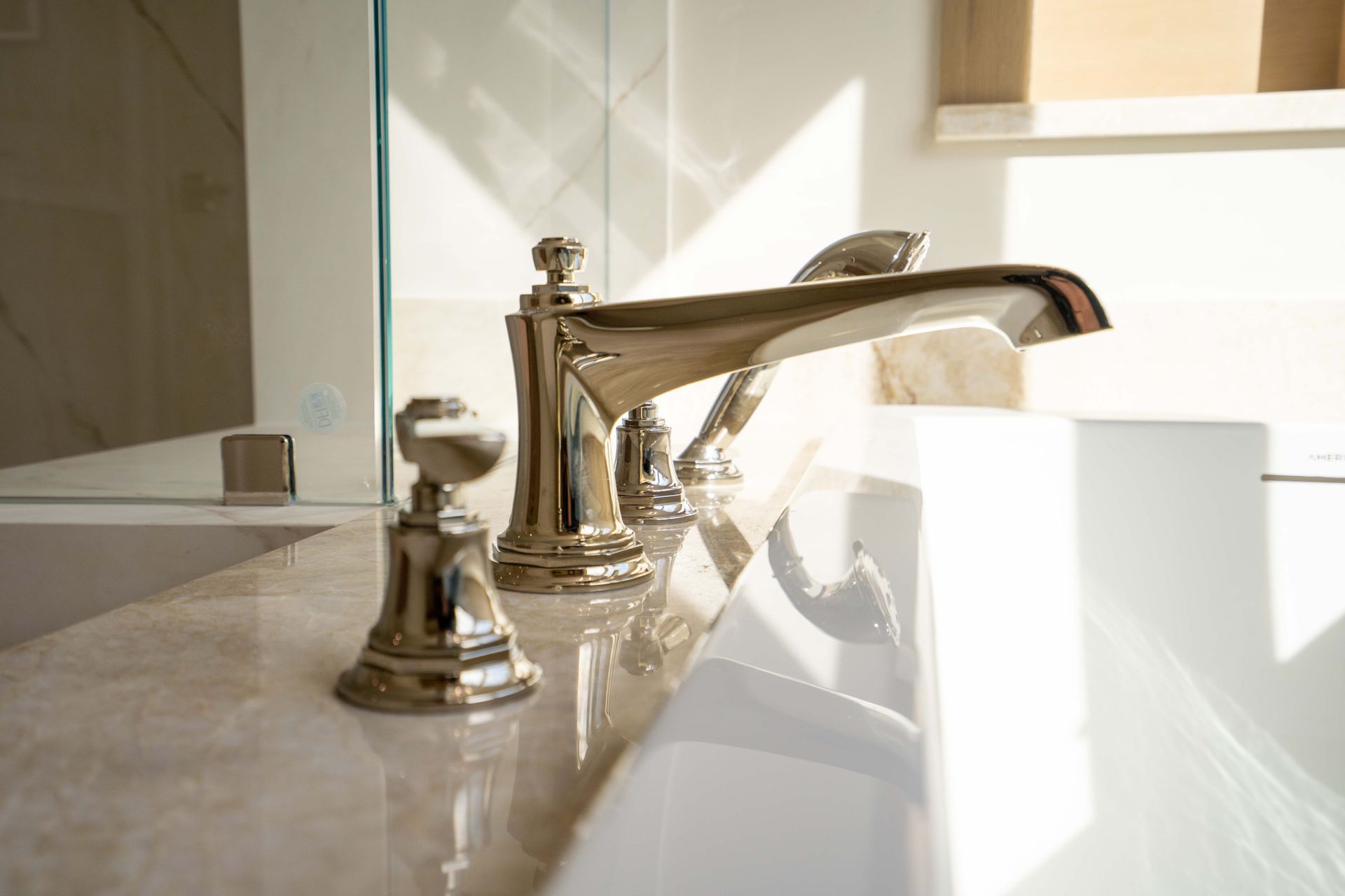 Shiny faucet on a light-colored countertop, bathroom setting. Sunlight creates reflections.