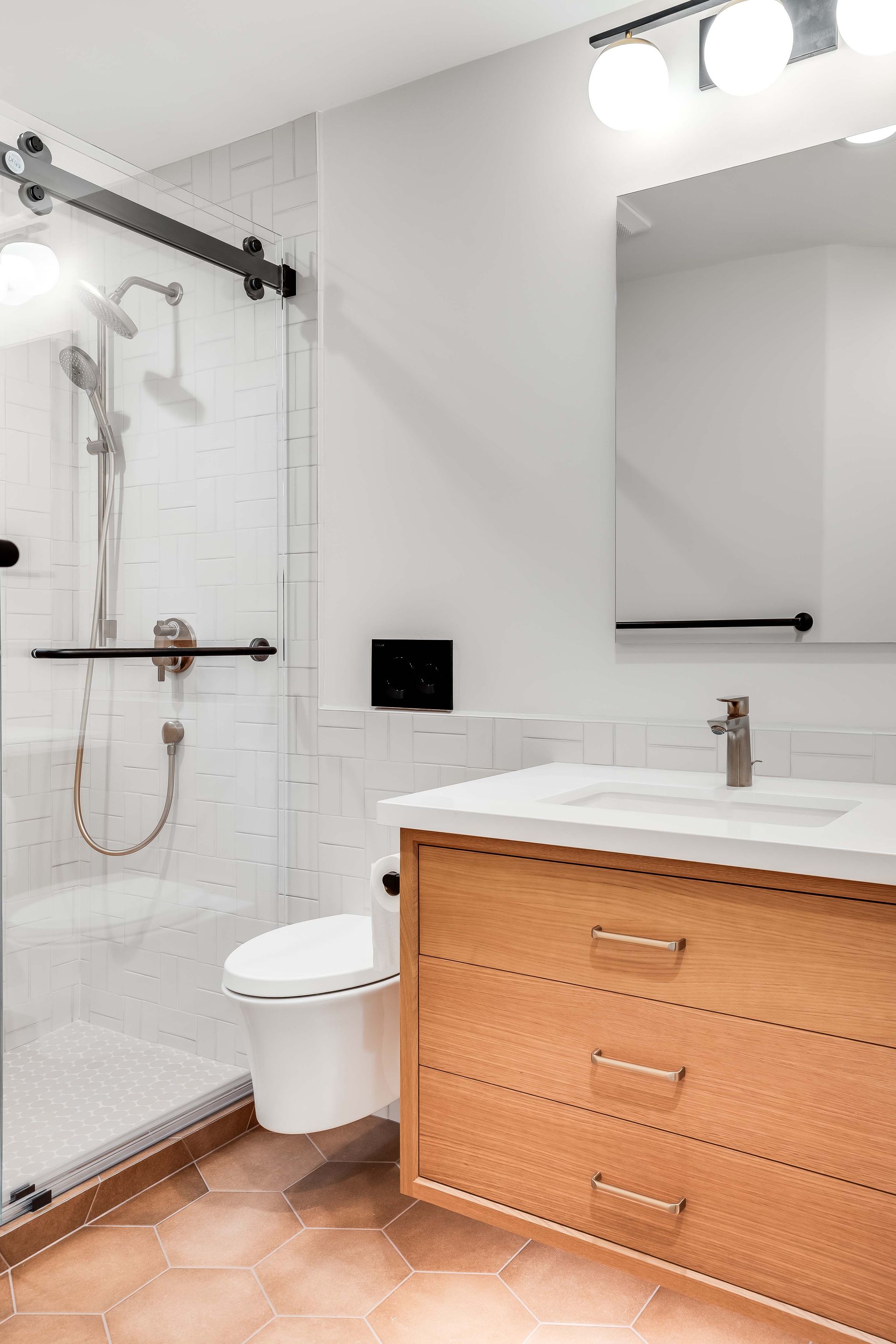 Modern bathroom with a glass shower, wooden vanity, white walls, and brown hexagonal floor tiles.