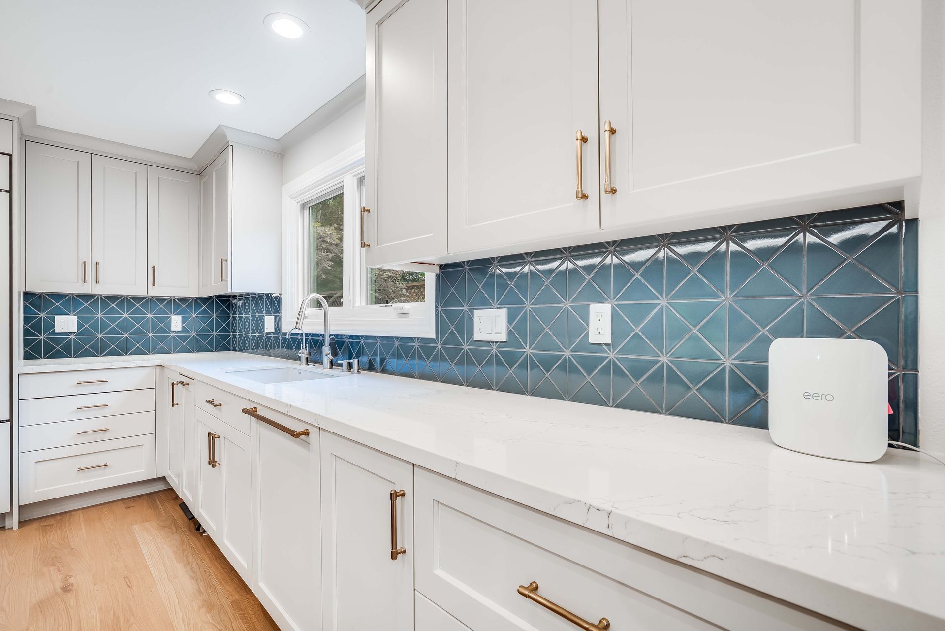 White kitchen with blue tile backsplash and gold hardware.