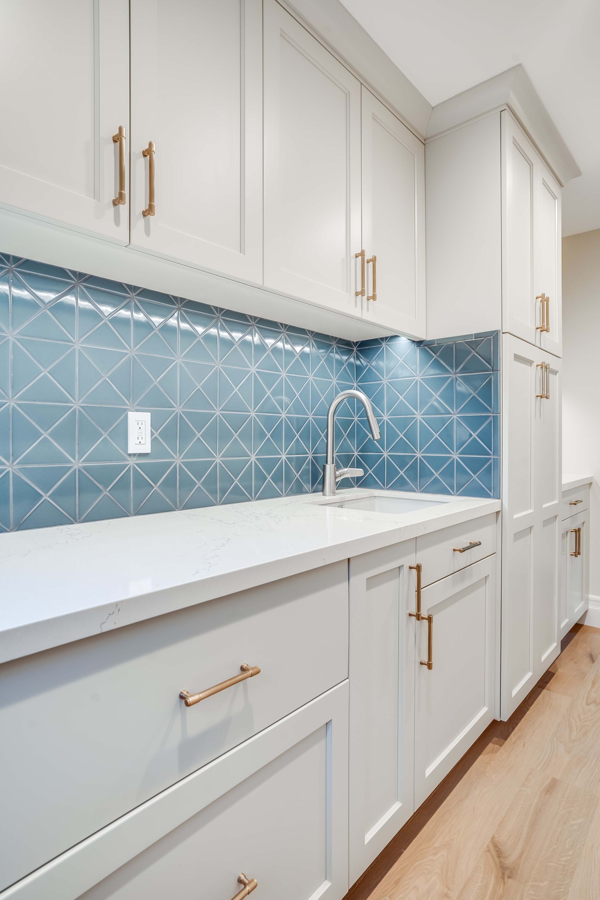 White cabinetry and countertop with blue geometric tile backsplash and gold hardware.
