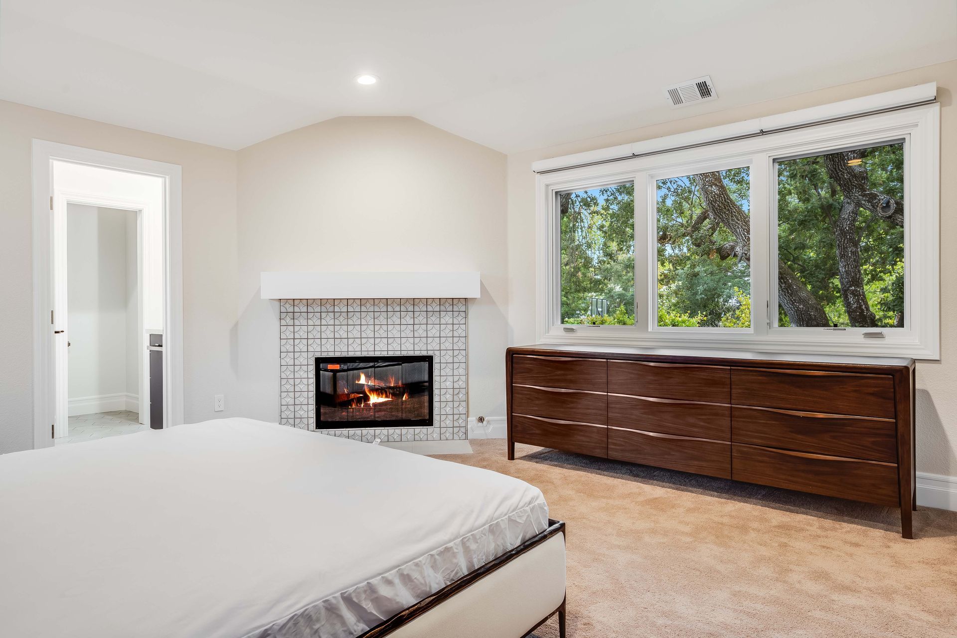 Bedroom with fireplace, window with view of trees, and wooden dresser.