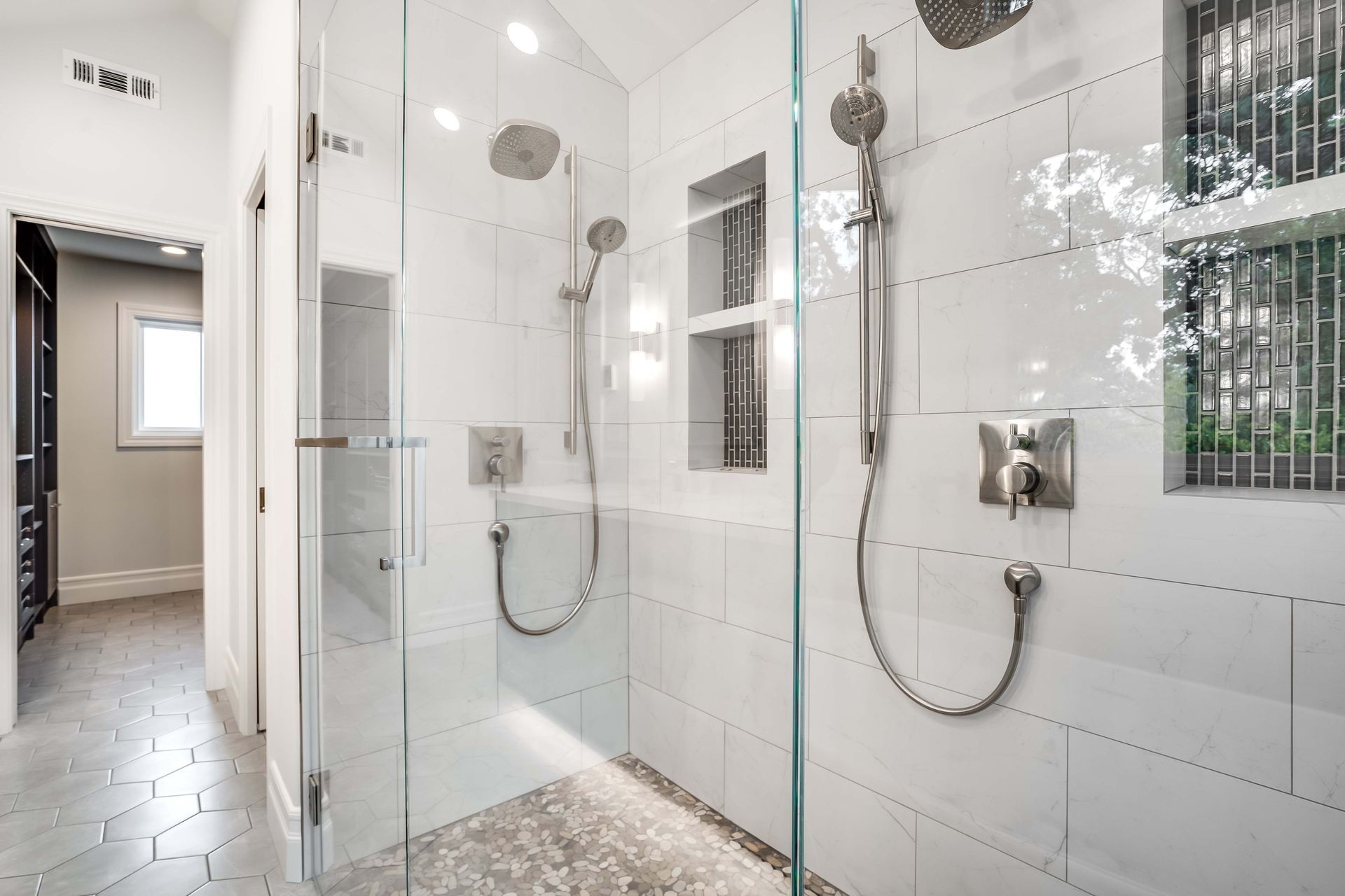 Modern white tile shower with two showerheads, glass doors, and pebble floor.