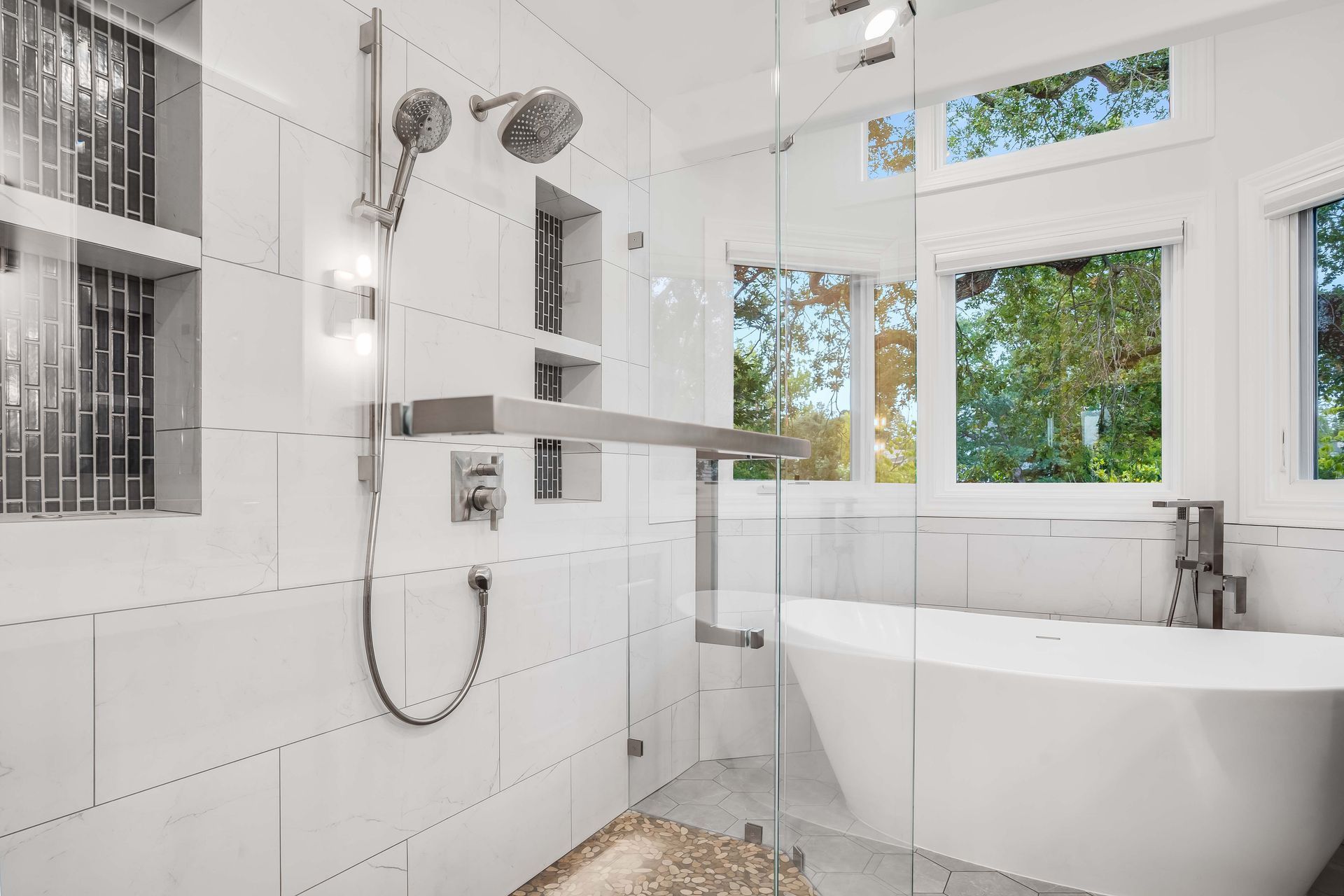 Modern bathroom with white tiled walls, glass shower door, and standalone tub by a window.