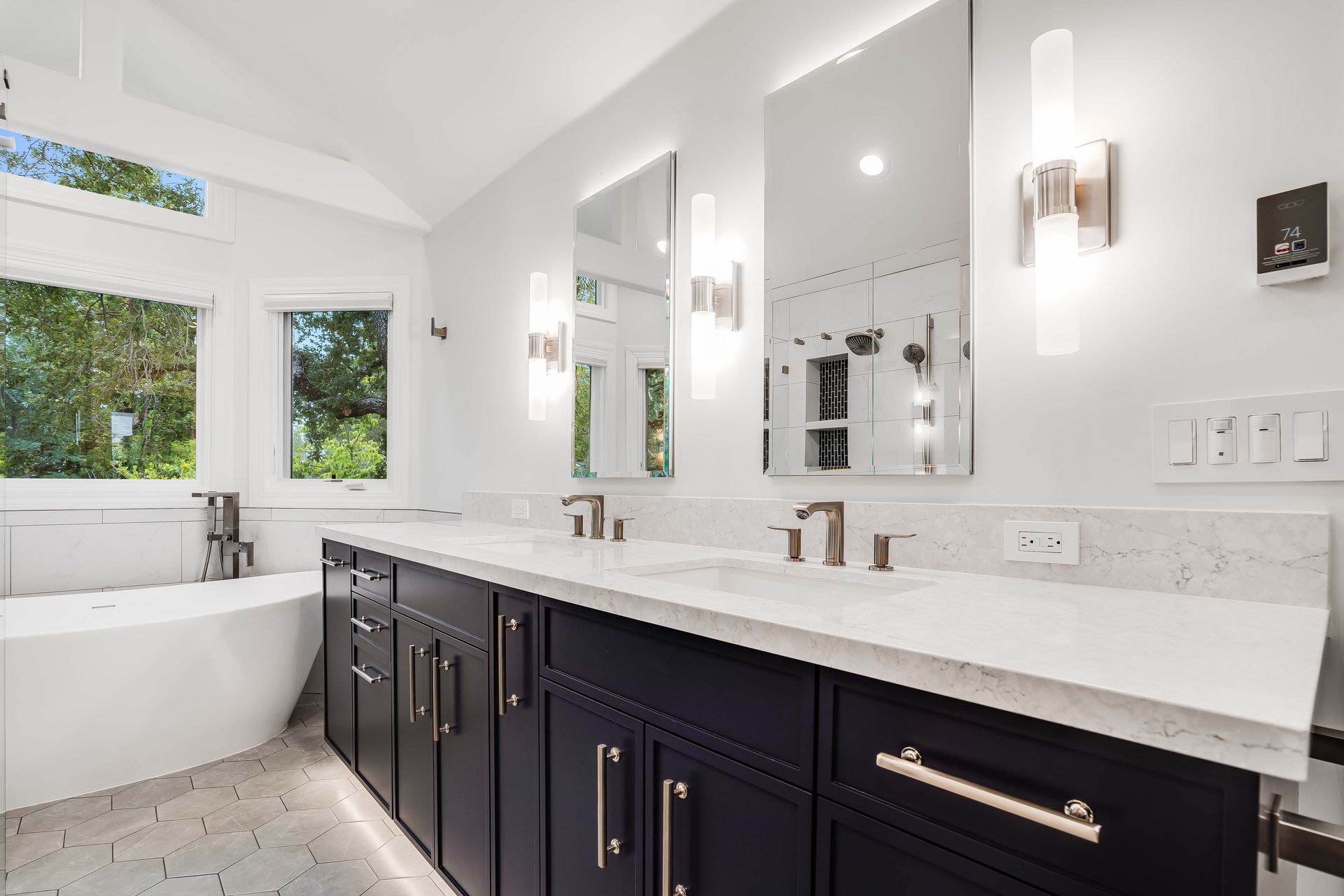 Modern bathroom with navy cabinets, white countertops, large mirrors, and a tub.