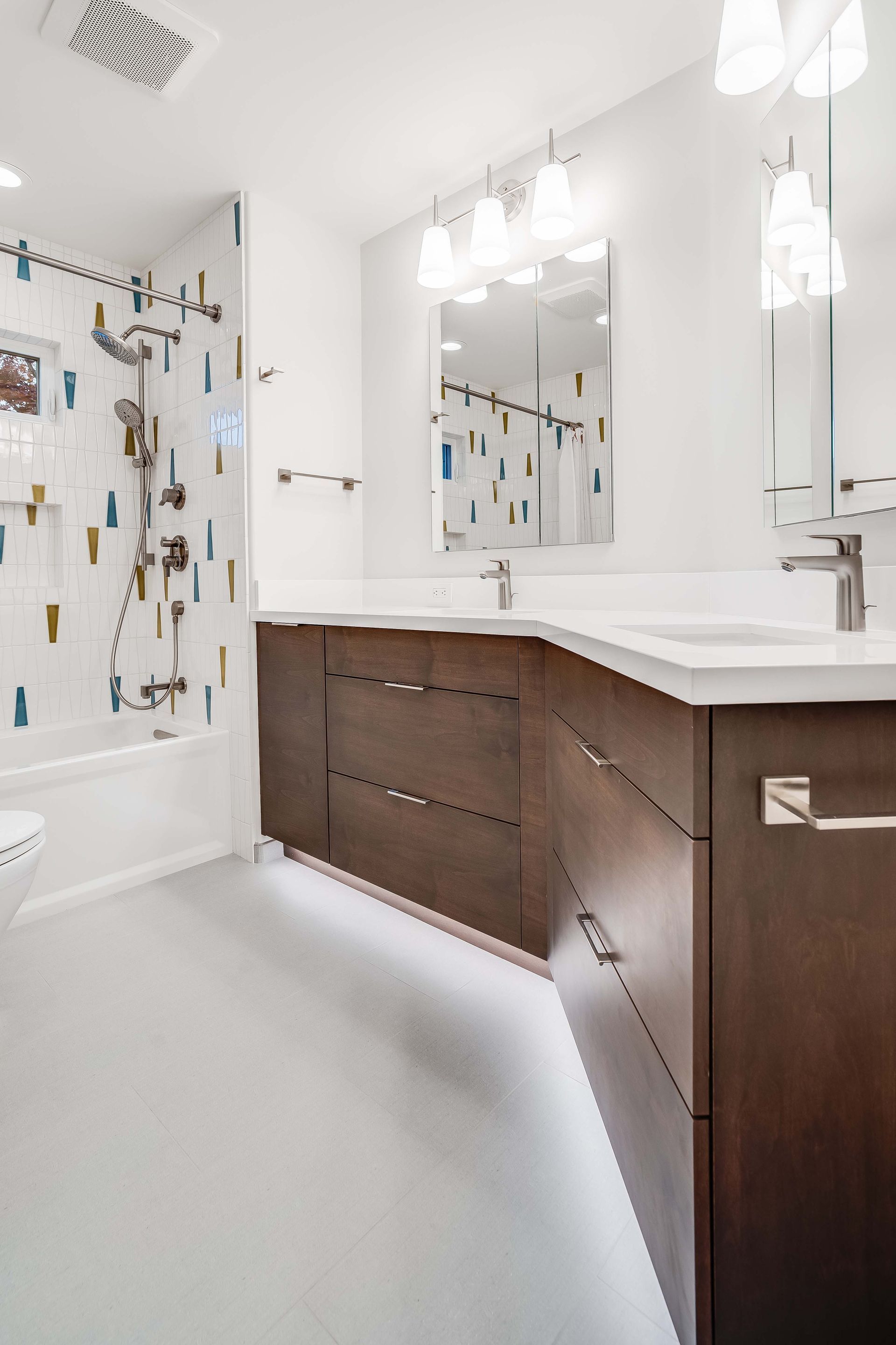Modern bathroom with a brown vanity, white countertops, and colorful tile in the shower.