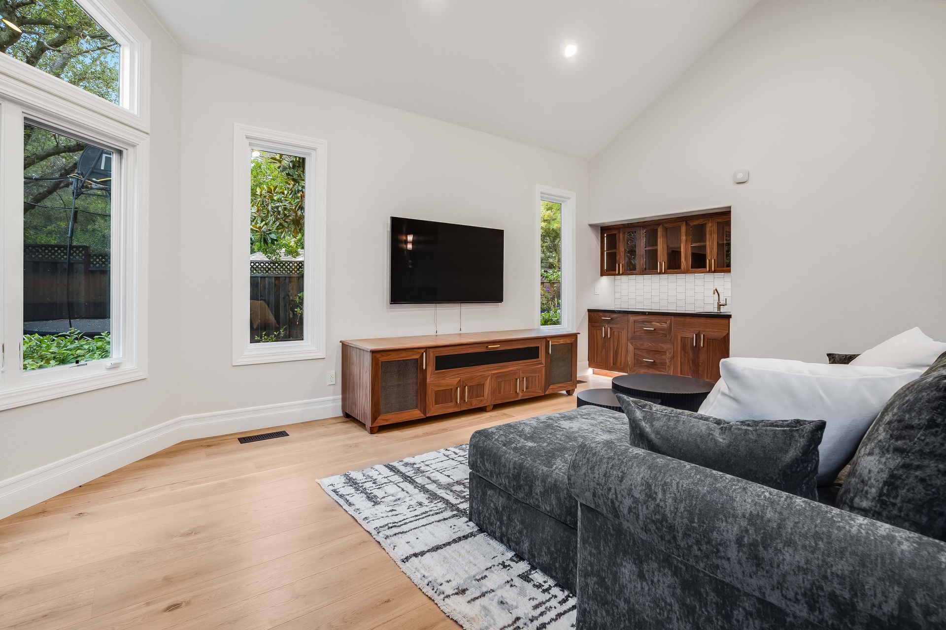 Living room with TV on wooden console, windows, and gray sectional sofa.