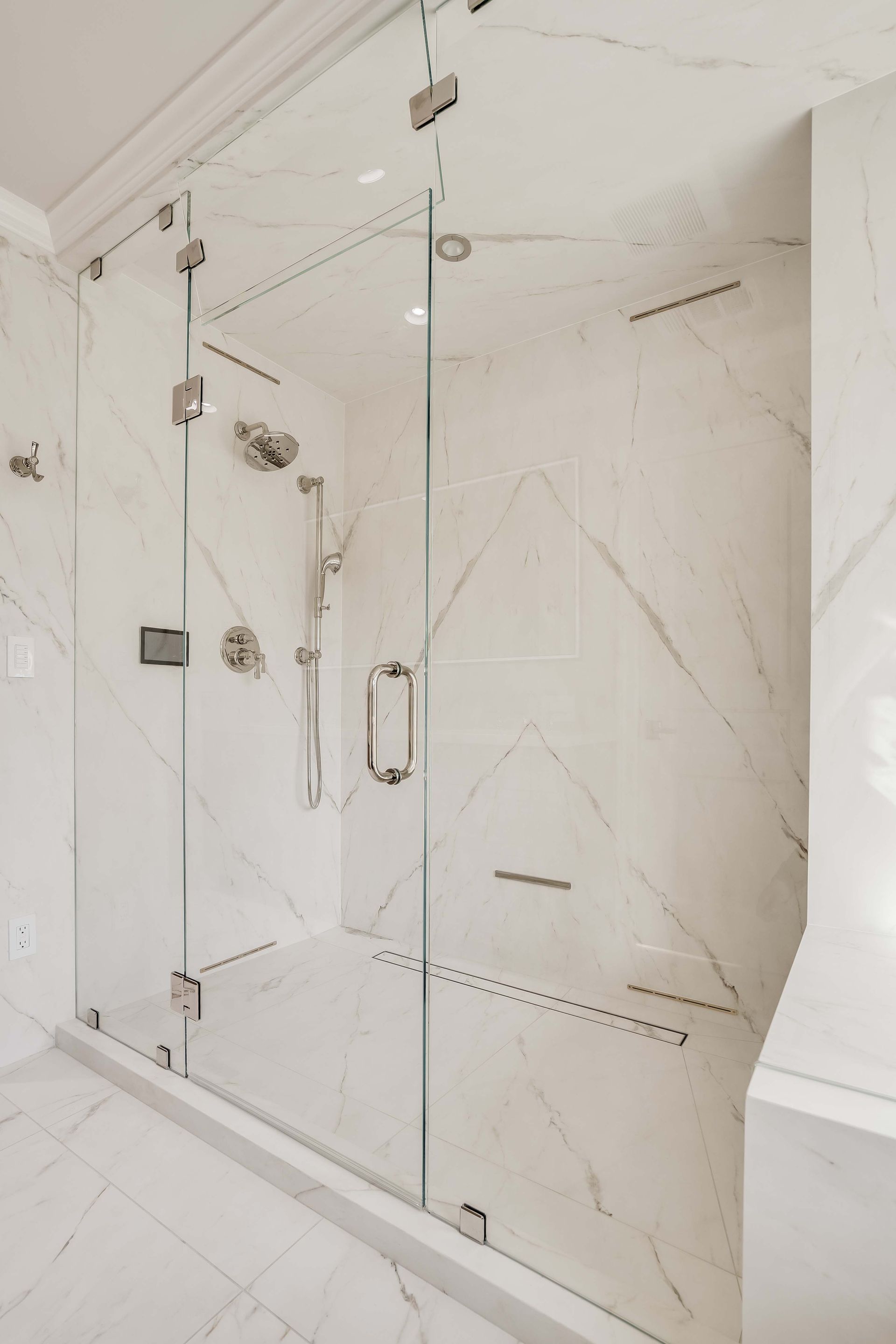 Glass-enclosed shower with white marble walls and silver fixtures.