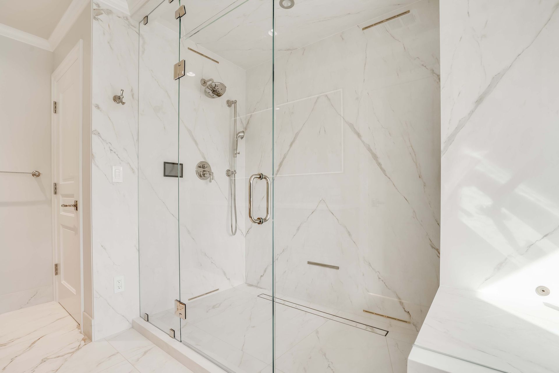 Spacious marble bathroom with glass shower. Shower has rain head and handheld, chrome fixtures.