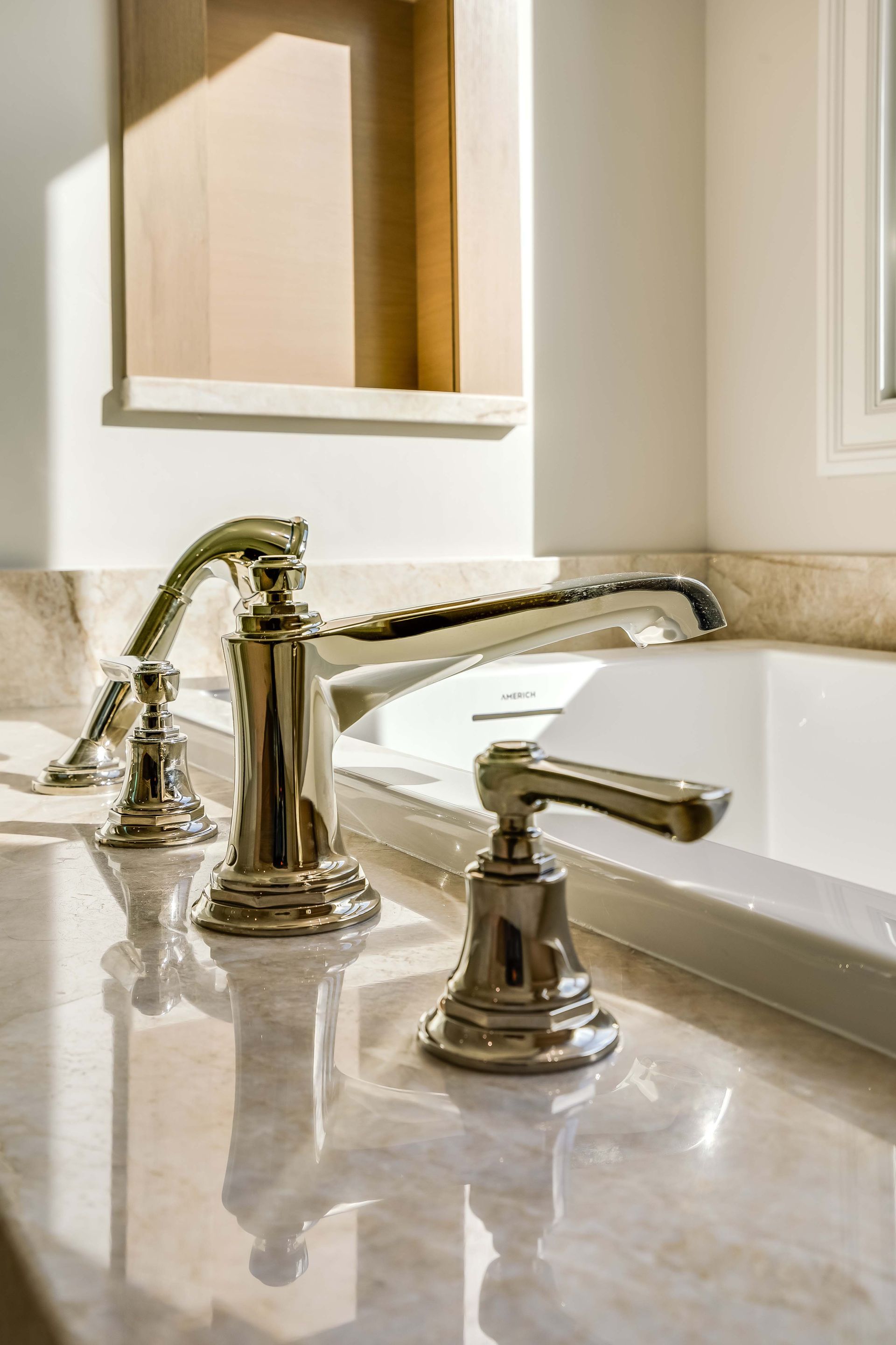 Shiny chrome bathtub faucet on a marble countertop with a built-in shelf in a bathroom.