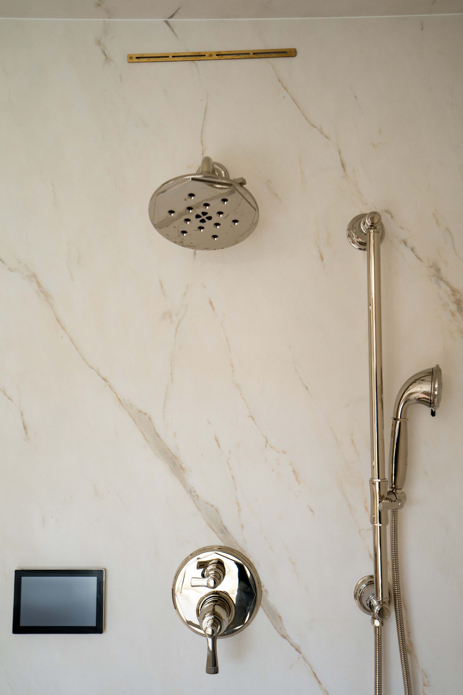 Shower wall with marble-like pattern. Includes shower head, controls, and handheld shower with bar on a light-colored wall.