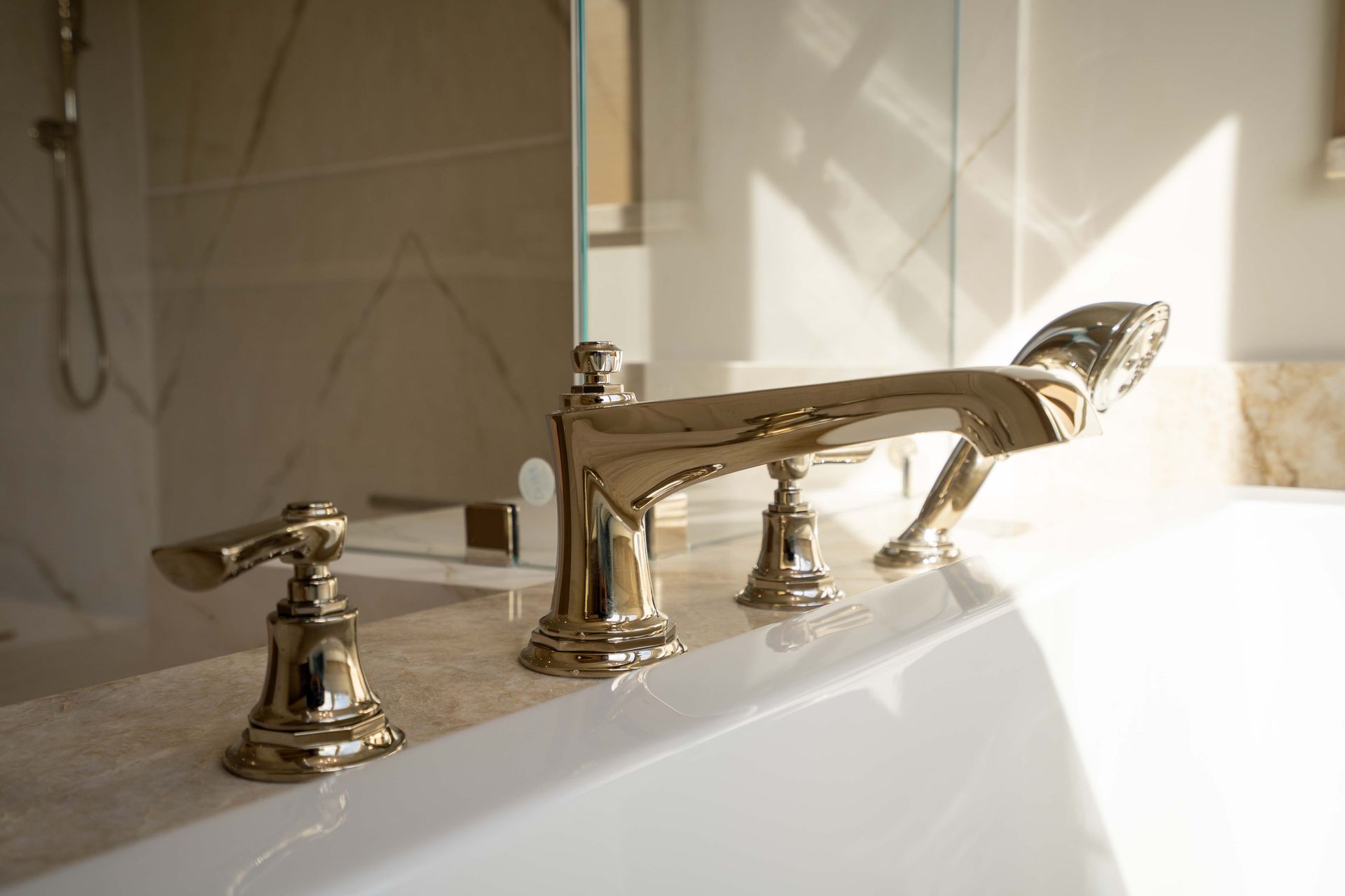 Shiny gold bathtub faucet against a white tub and marble wall.