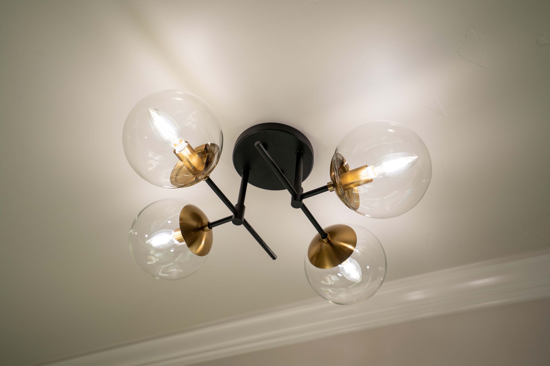 Black and brass ceiling light with four glass globe shades; lit against a white ceiling.