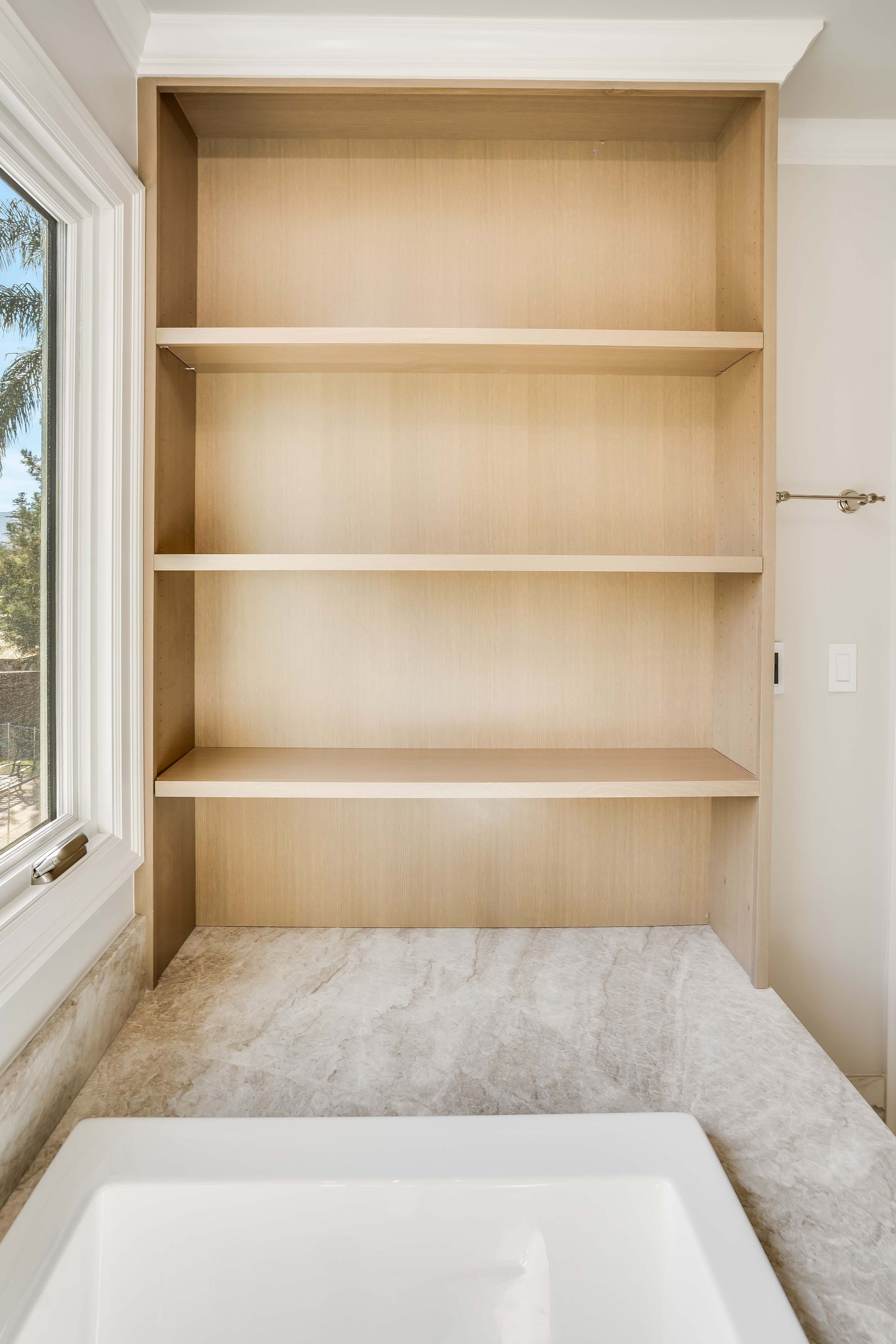Built-in wooden shelves in a bathroom above a countertop and next to a window.